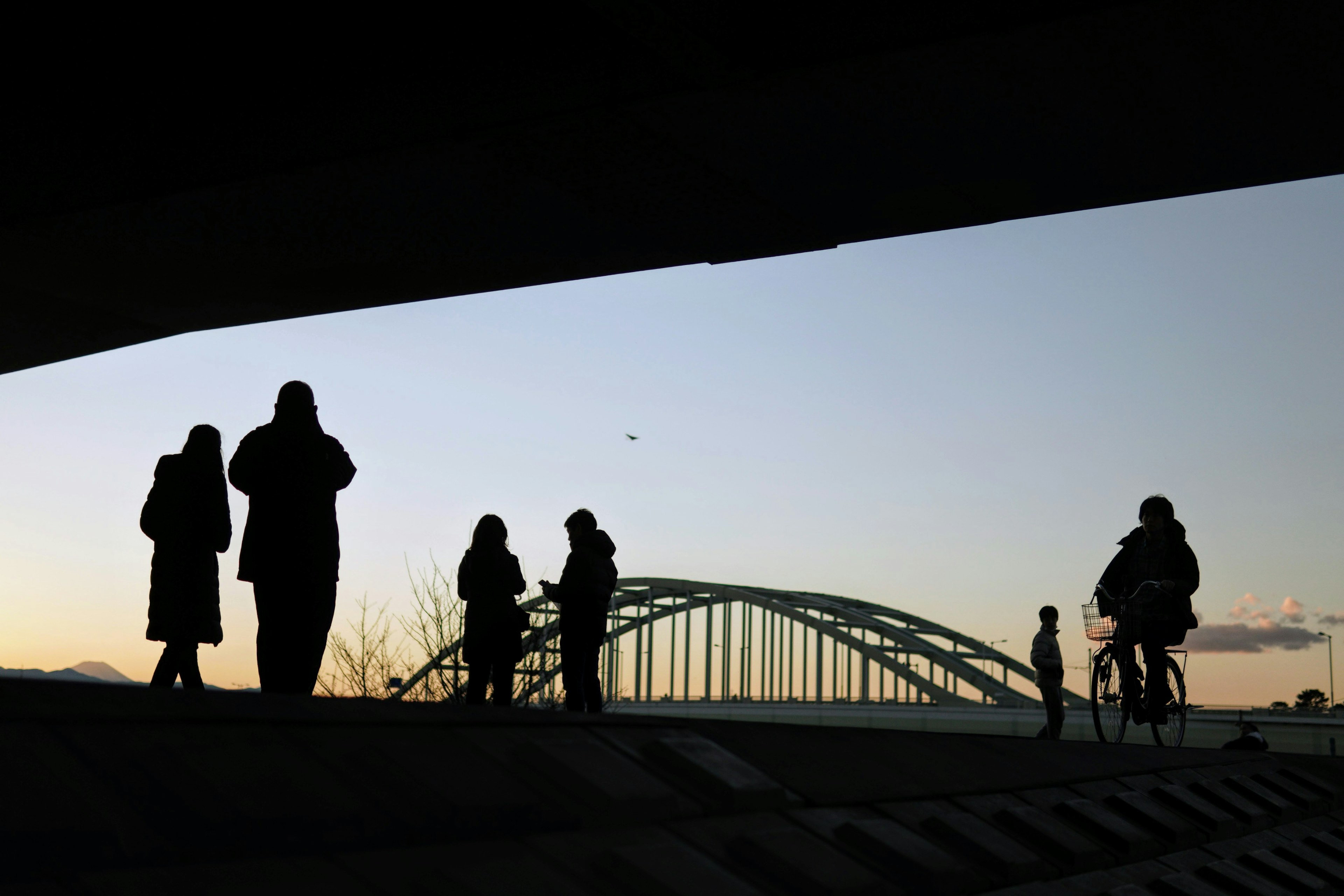 Silhouettes de personnes marchant sous un pont au coucher du soleil