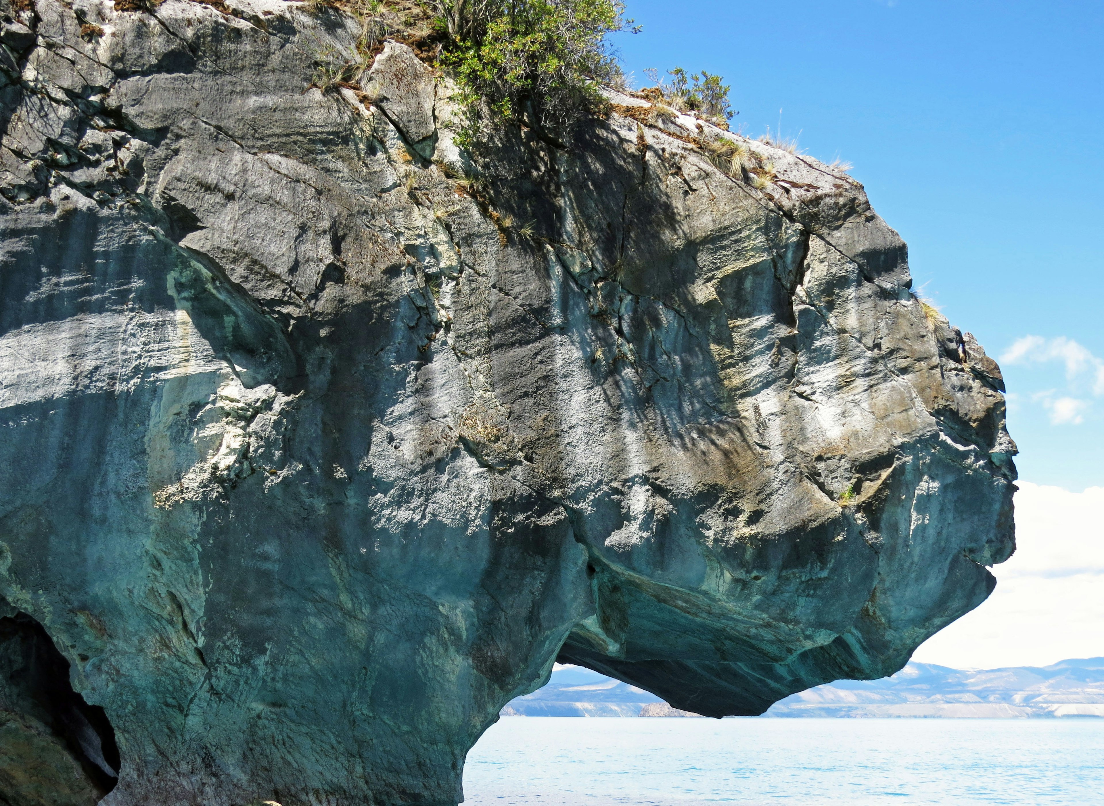 Large rock formation emerging from blue water with visible layers on the surface