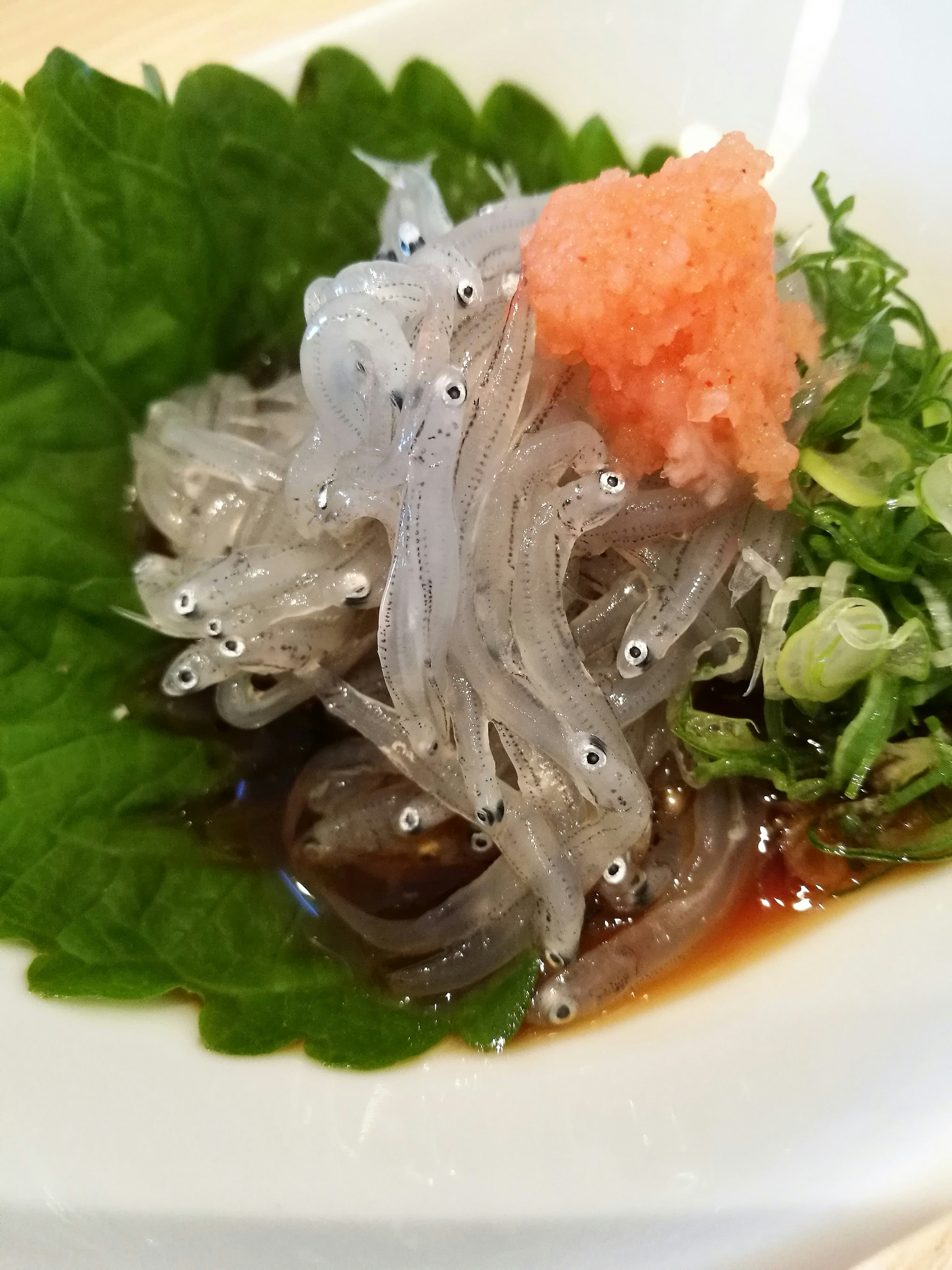 Dish featuring translucent small fish with green leaves and pink fish roe