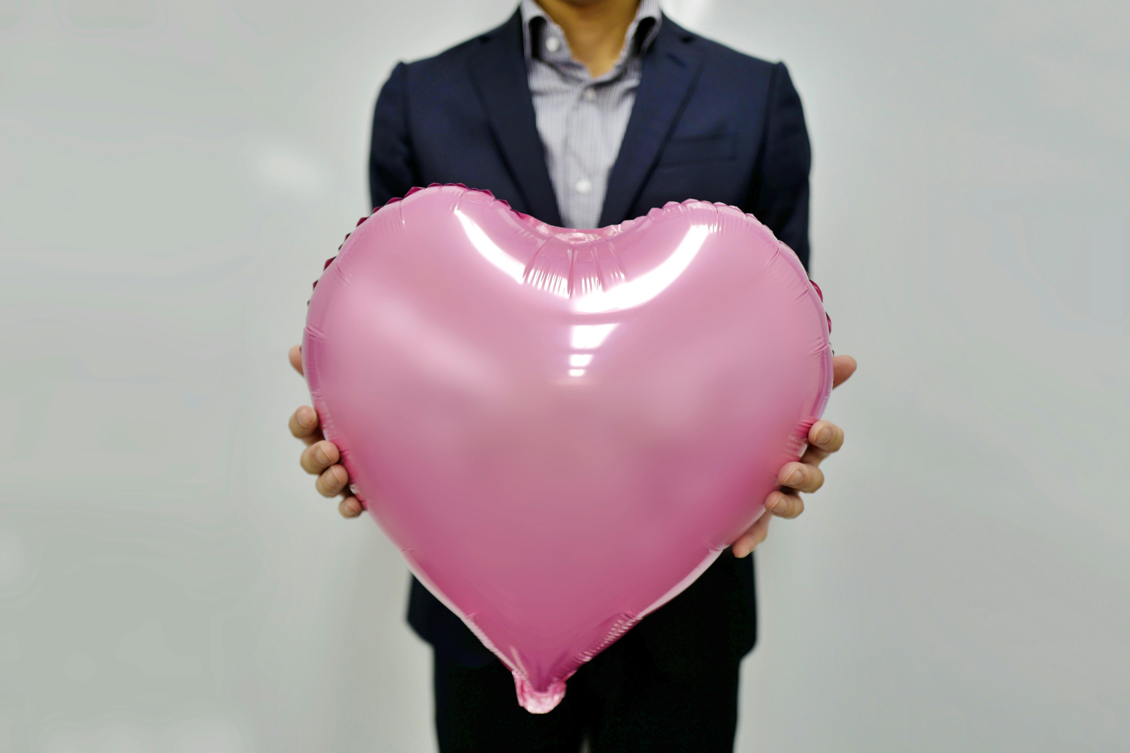 Un hombre con traje sosteniendo un globo en forma de corazón rosa