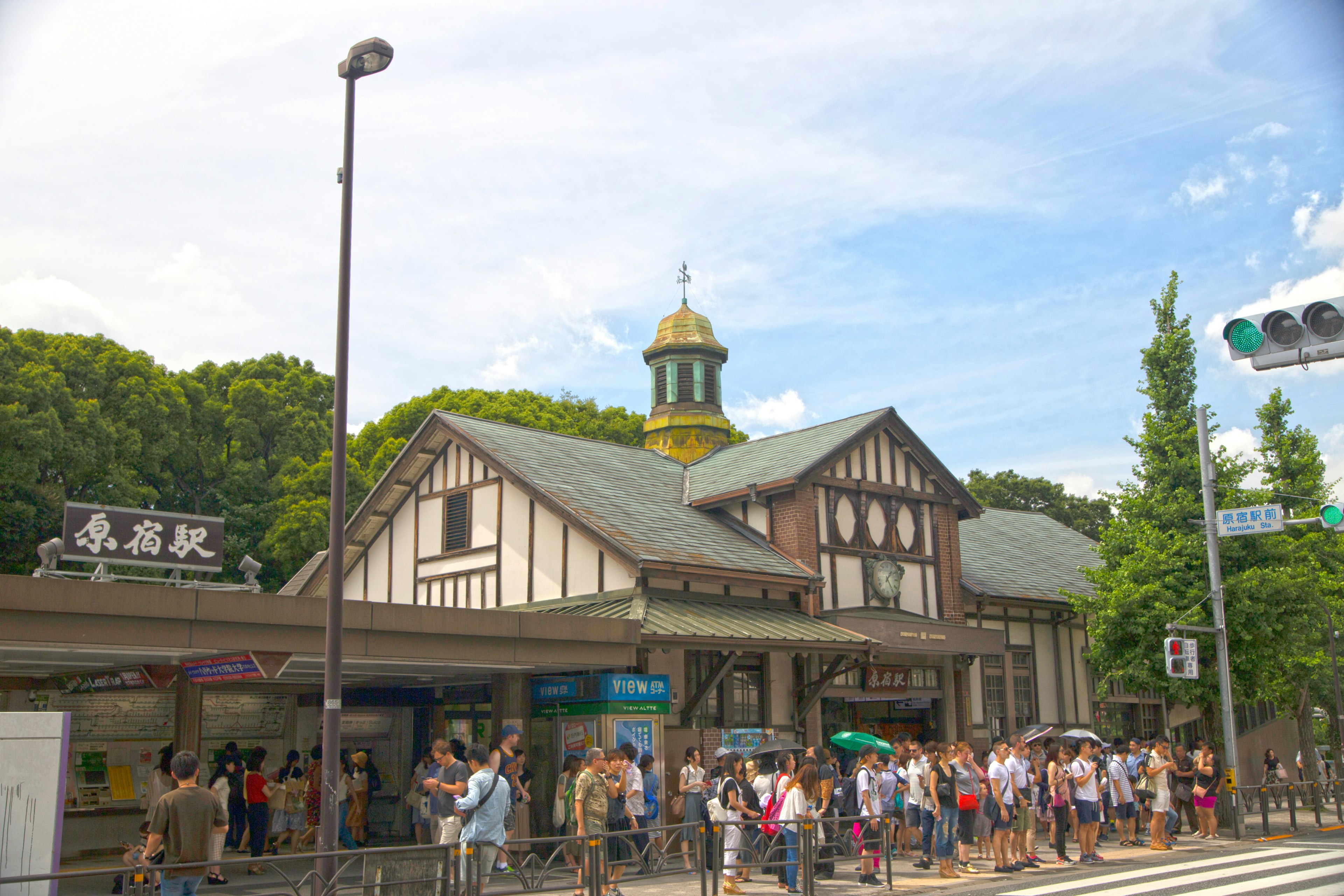 Exterior view of a busy train station with unique architectural style surrounded by greenery