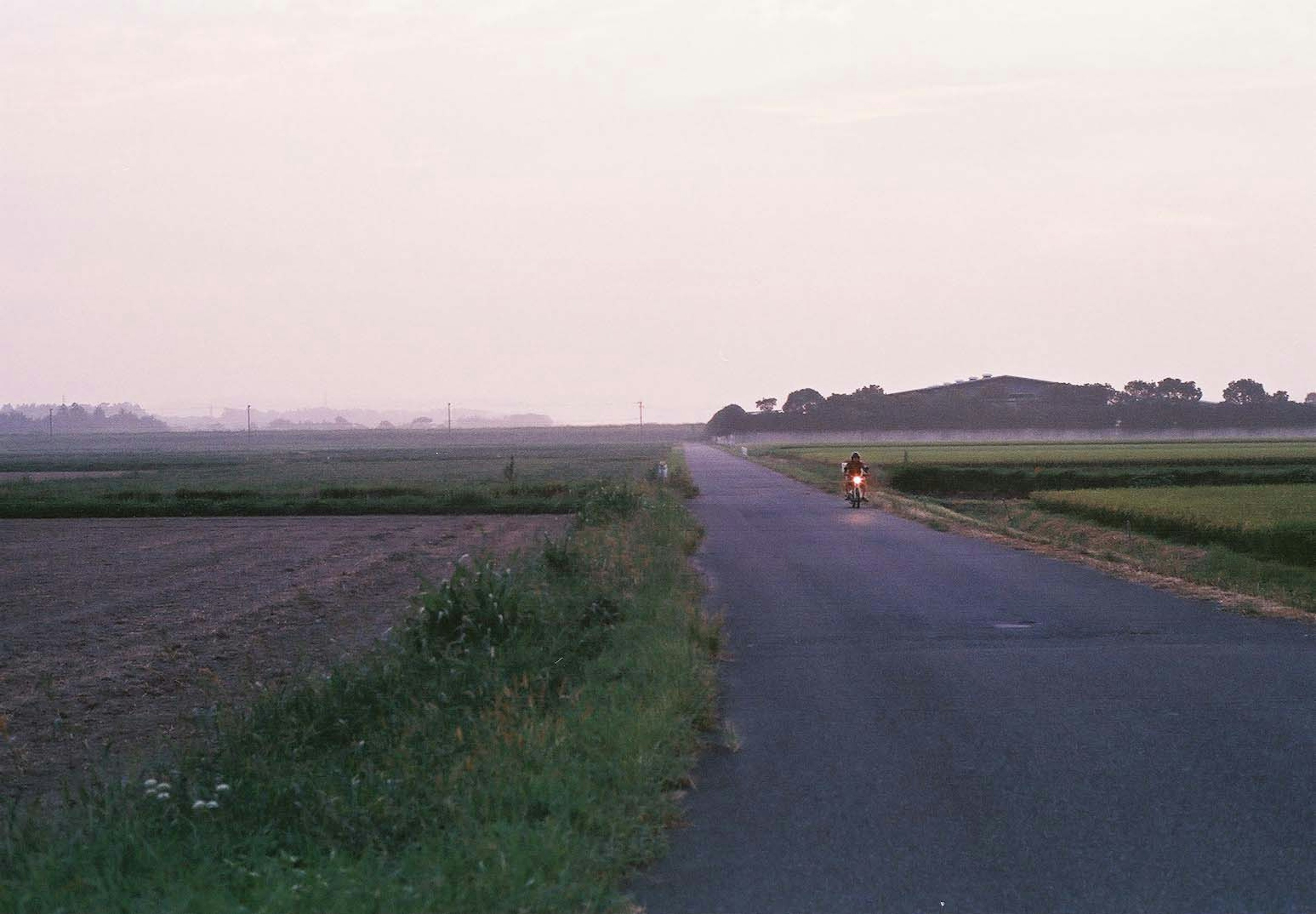 Jalan pedesaan dengan ladang luas dan bukit jauh