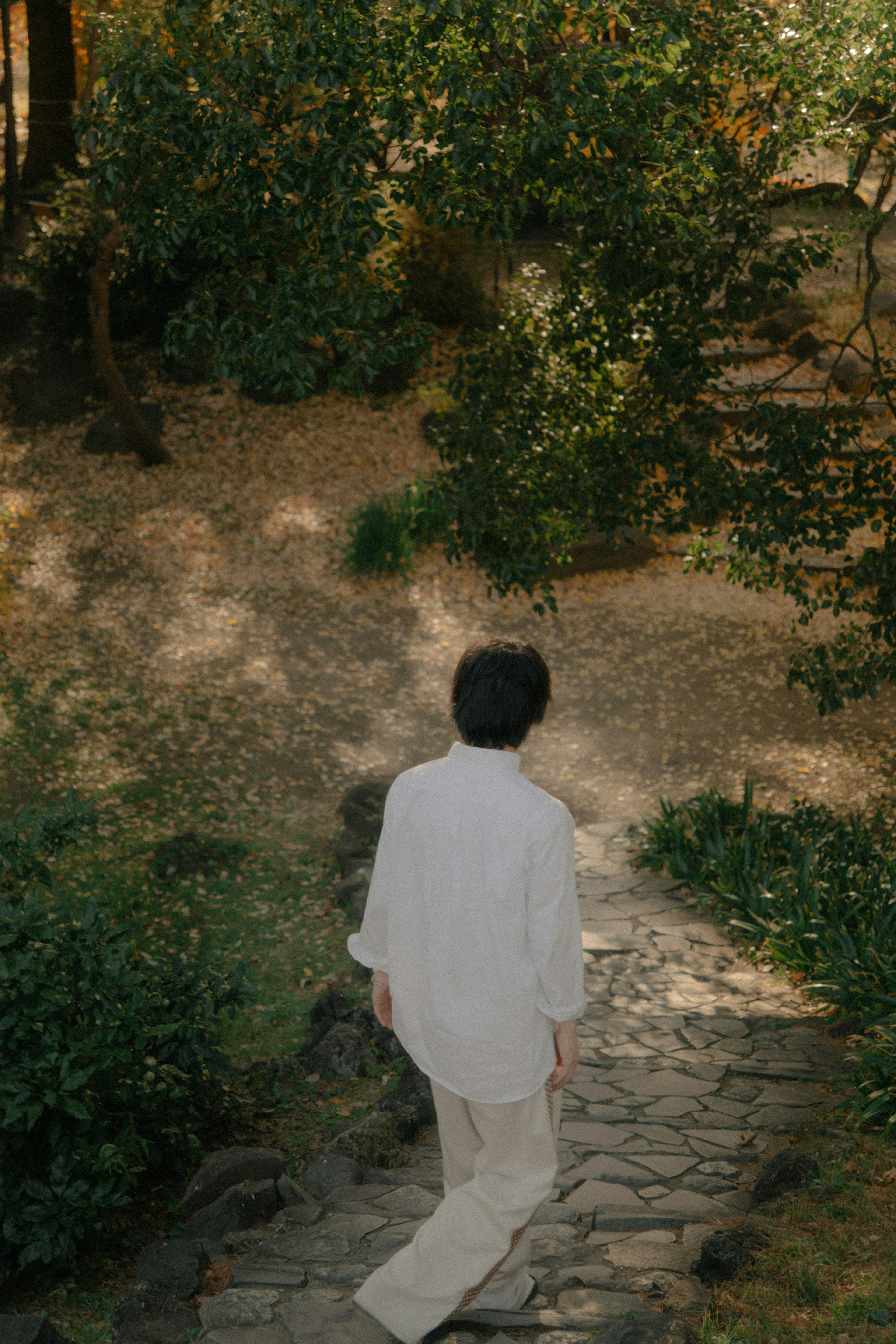 A person in white clothing walking on a stone path in a forest setting