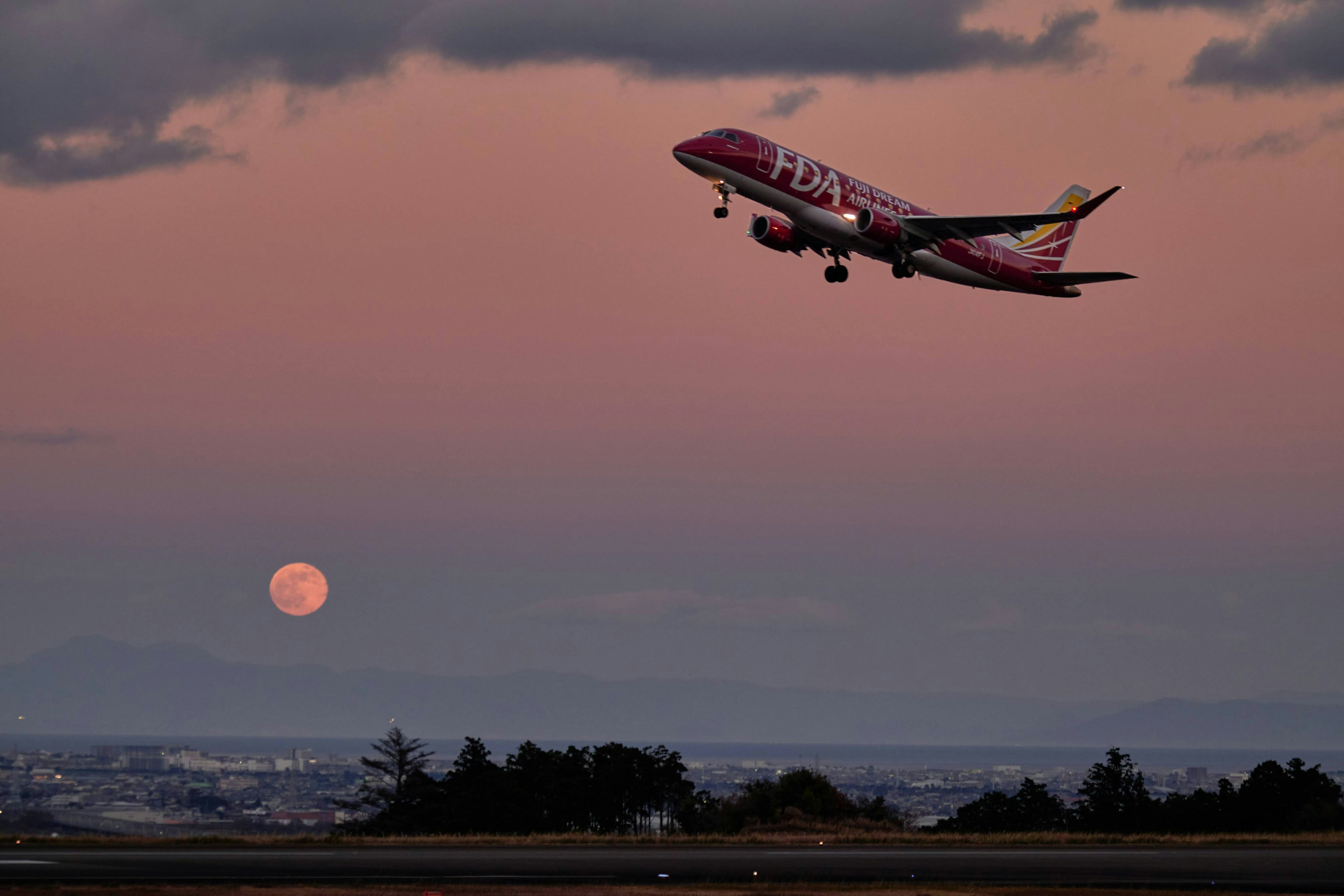 Avión despegando contra un cielo de atardecer con una luna llena