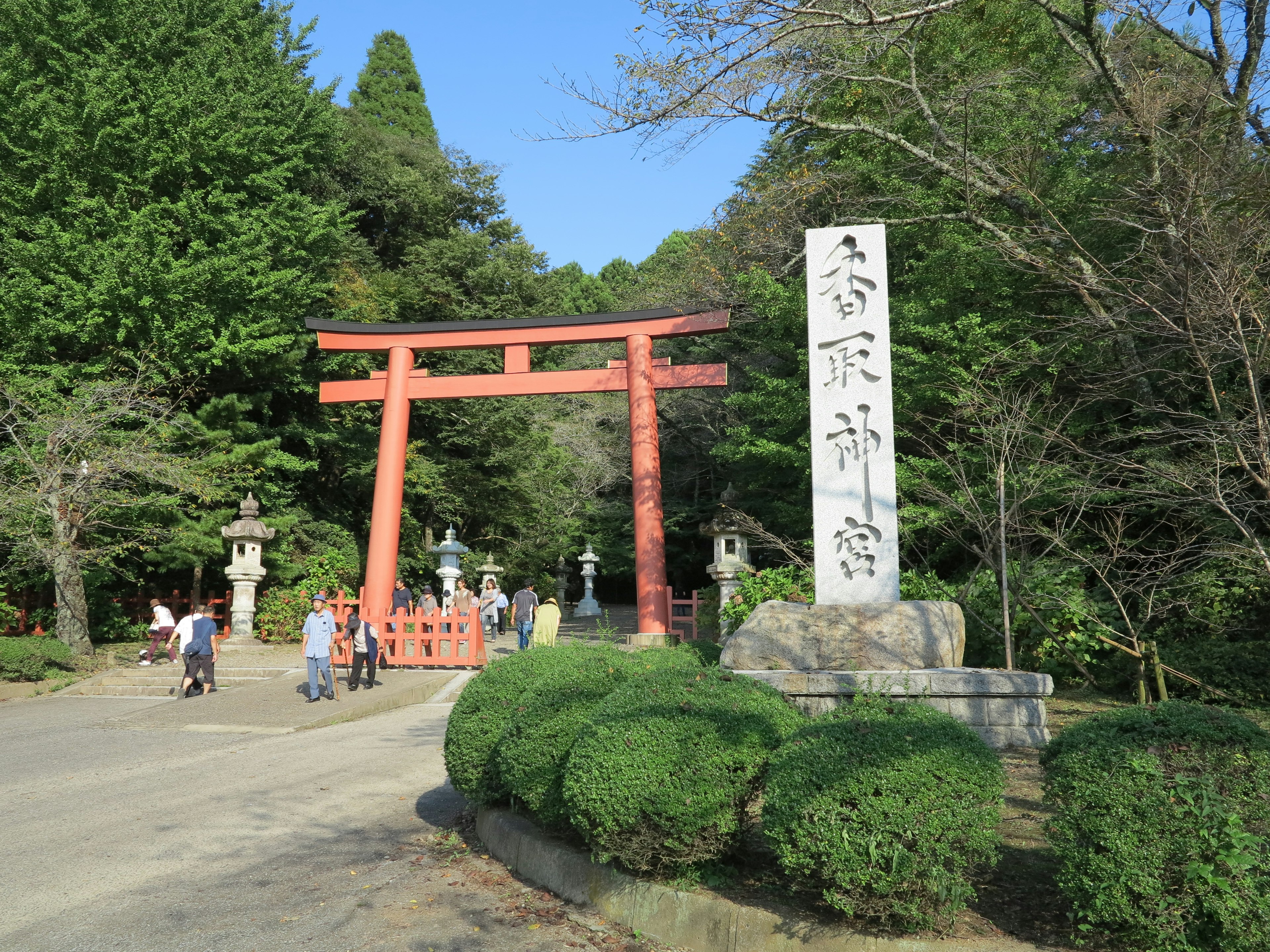 神社入口，紅色鳥居和石碑，遊客在散步