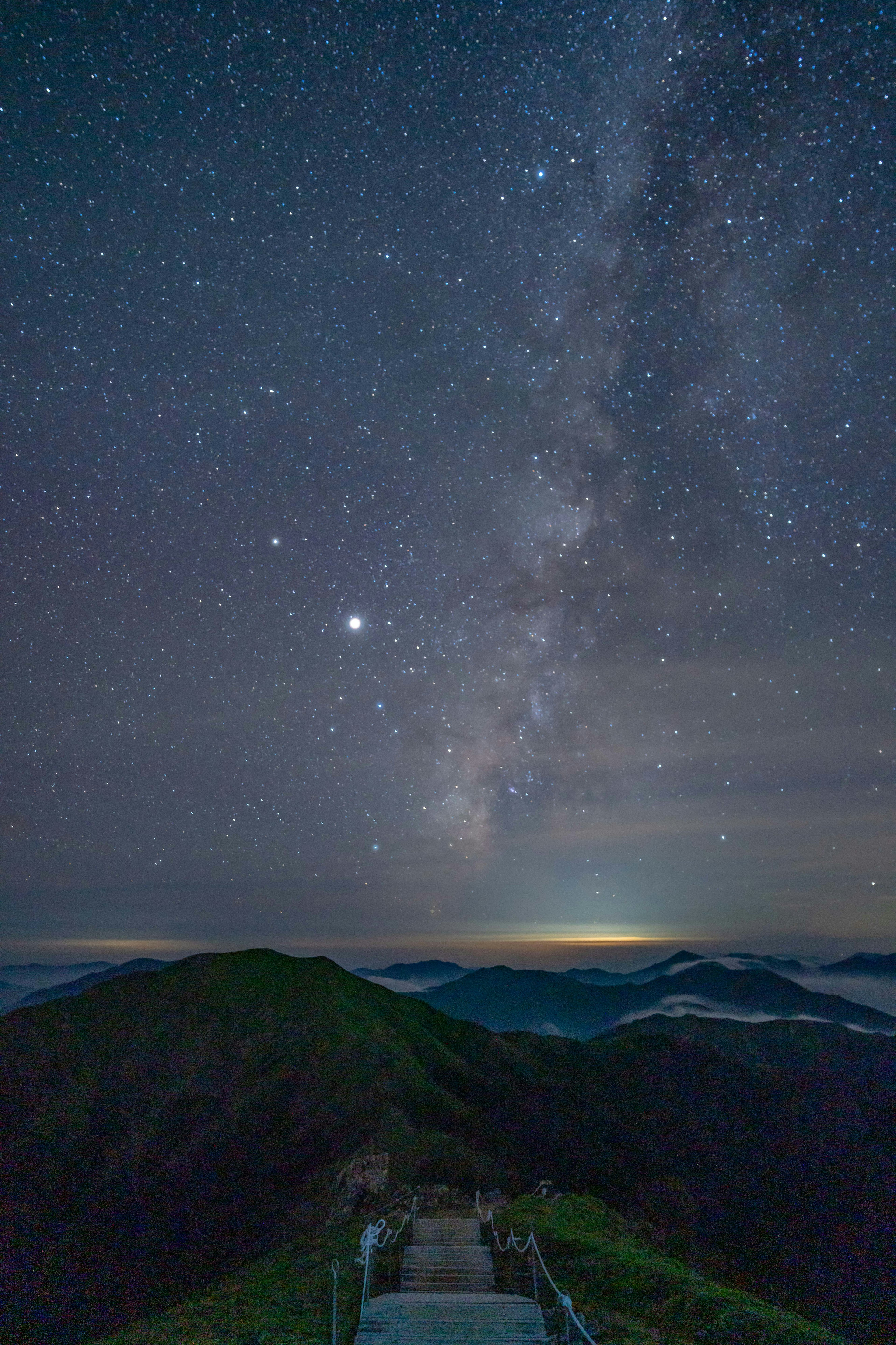 Paisaje montañoso con un cielo estrellado y la Vía Láctea visible Escaleras que conducen a la cima