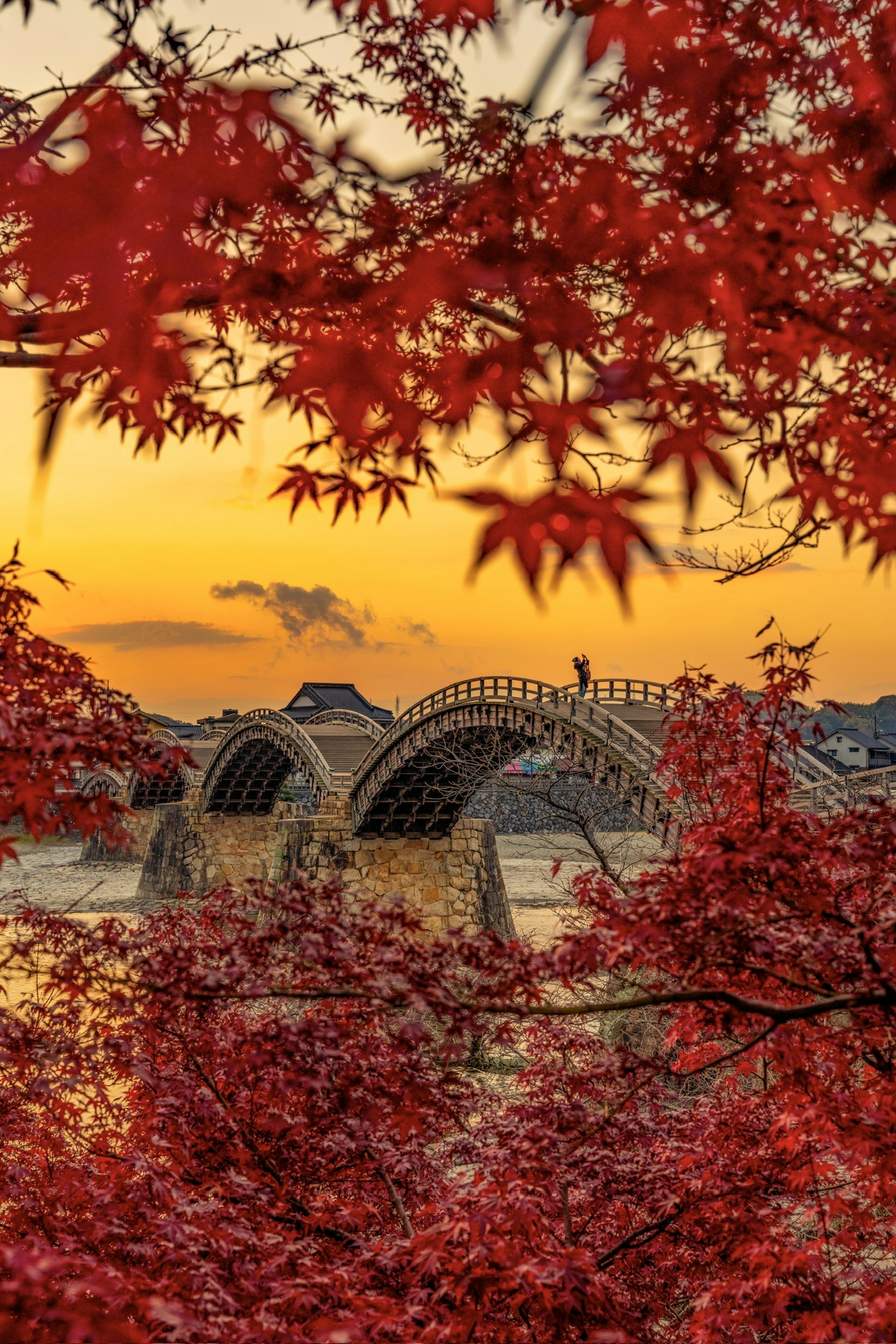 Schöner Brücke umgeben von roten Ahornblättern und Sonnenuntergang