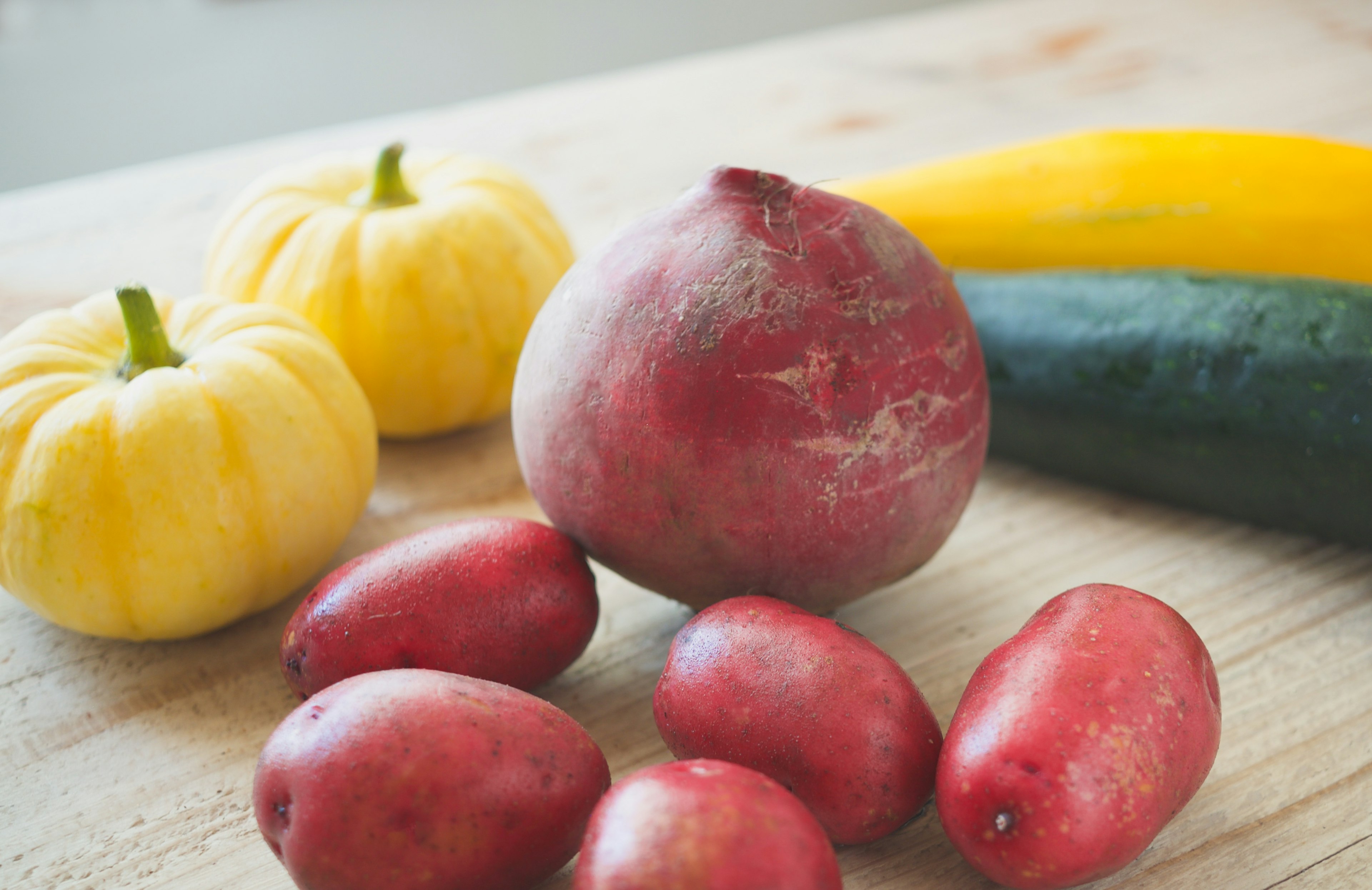 Verduras frescas dispuestas sobre una mesa de madera que incluyen calabacines verdes patatas rojas y calabazas amarillas