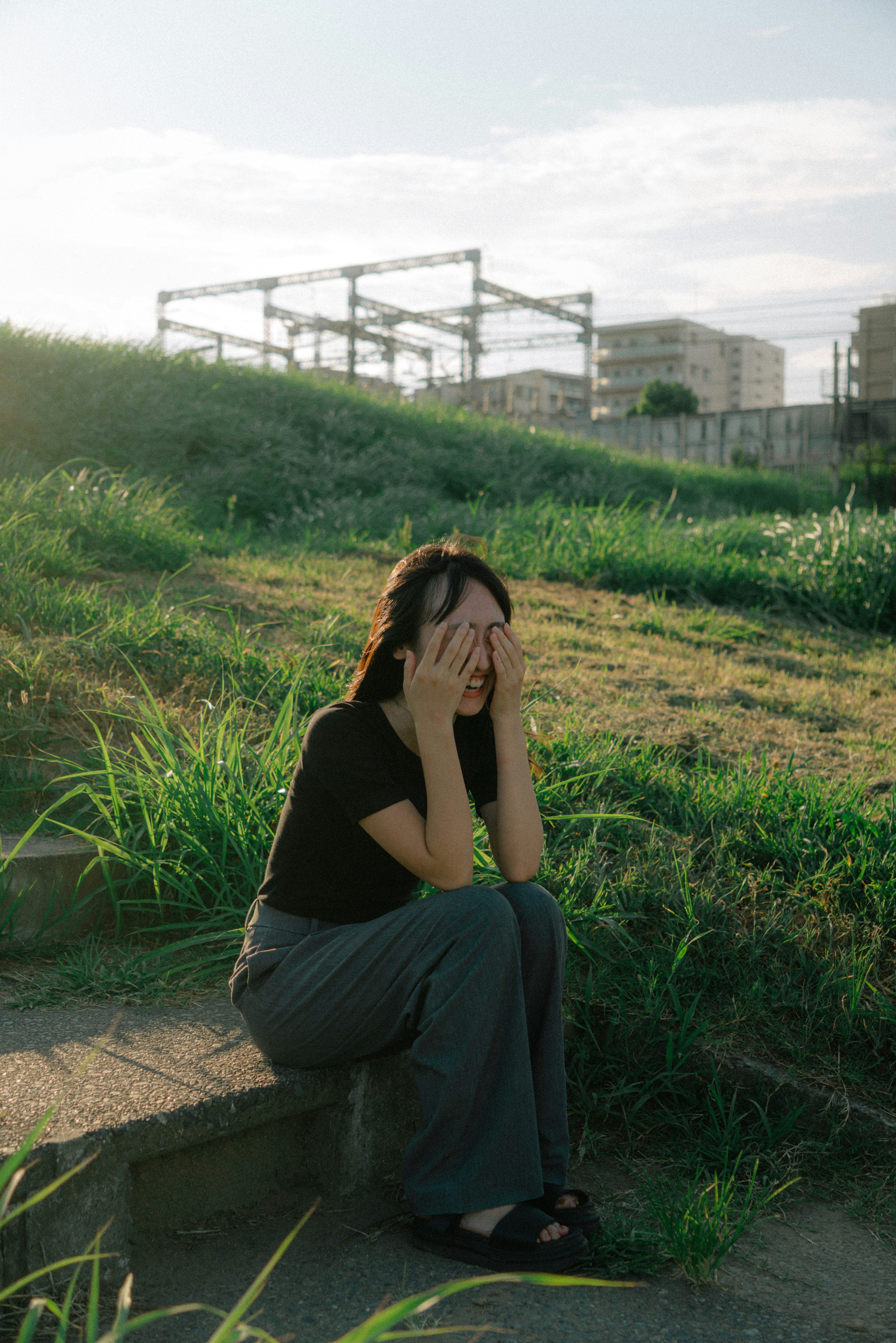 一位女性坐在草地上，用手遮住臉