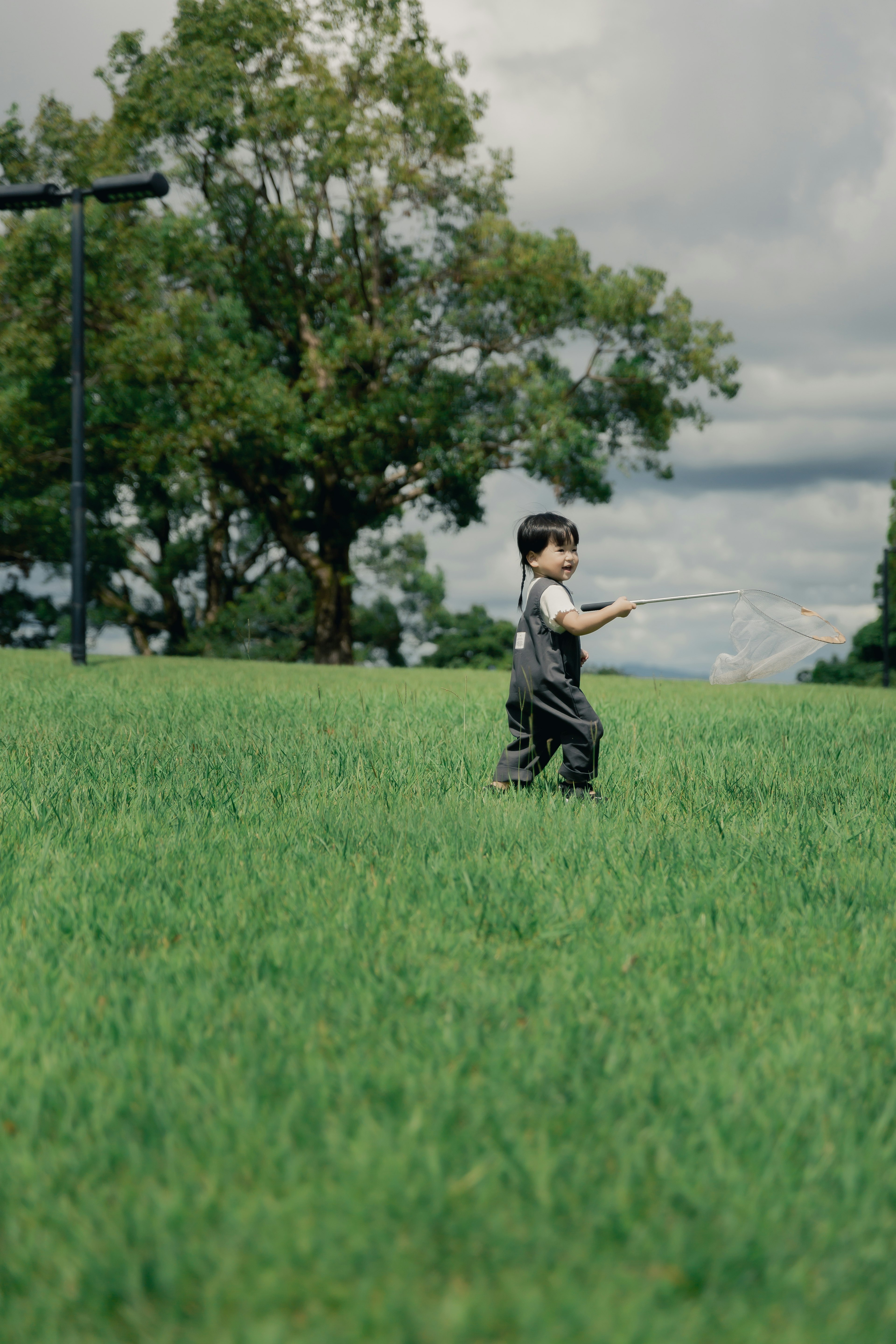 Bambino che cammina in un campo verde con alberi e cielo nuvoloso sullo sfondo