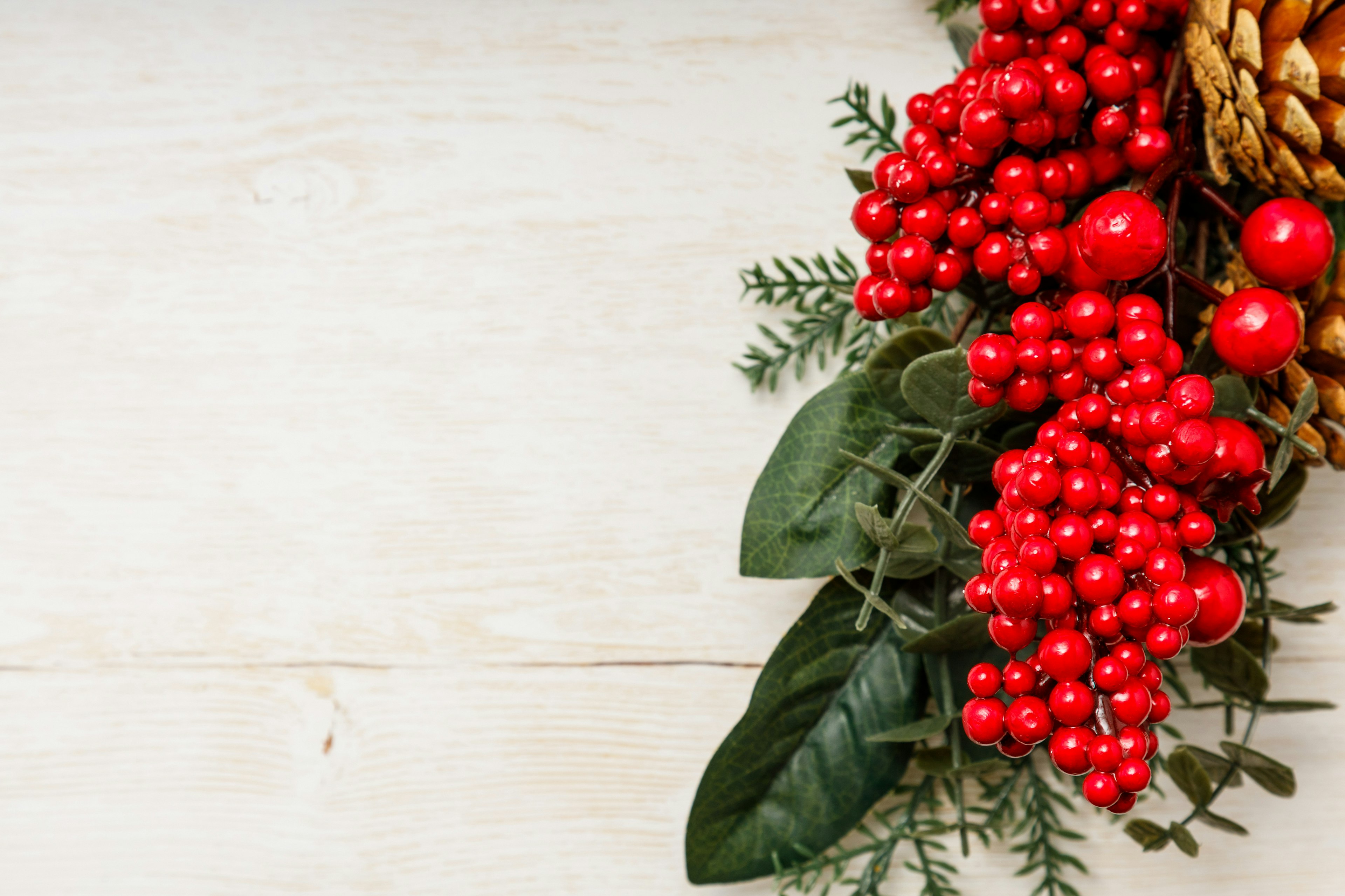 Christmas arrangement with red berries and pine cone on wooden table