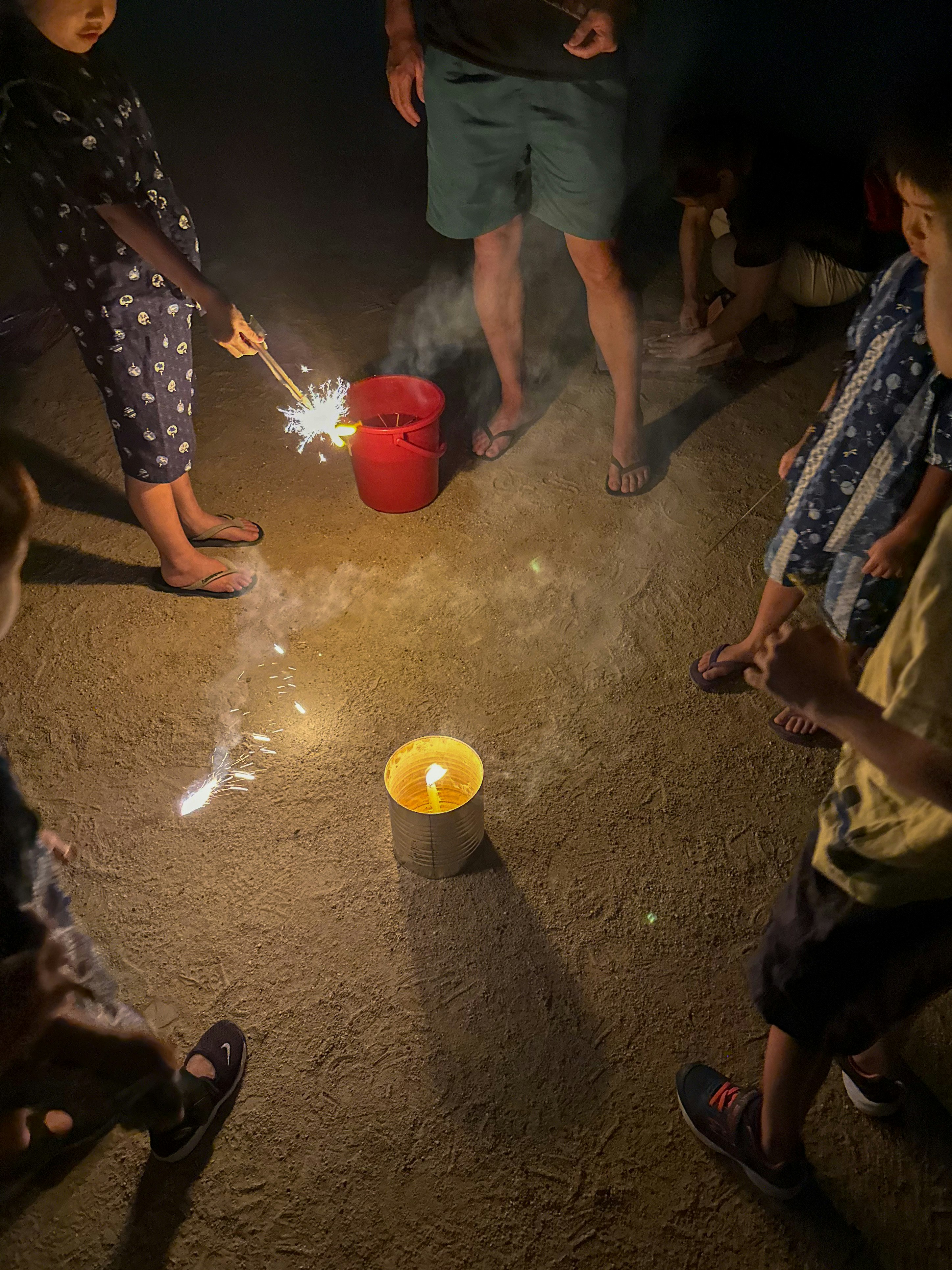 Kinder halten Wunderkerzen in einer Nachtszene und spielen um eine große Kerze