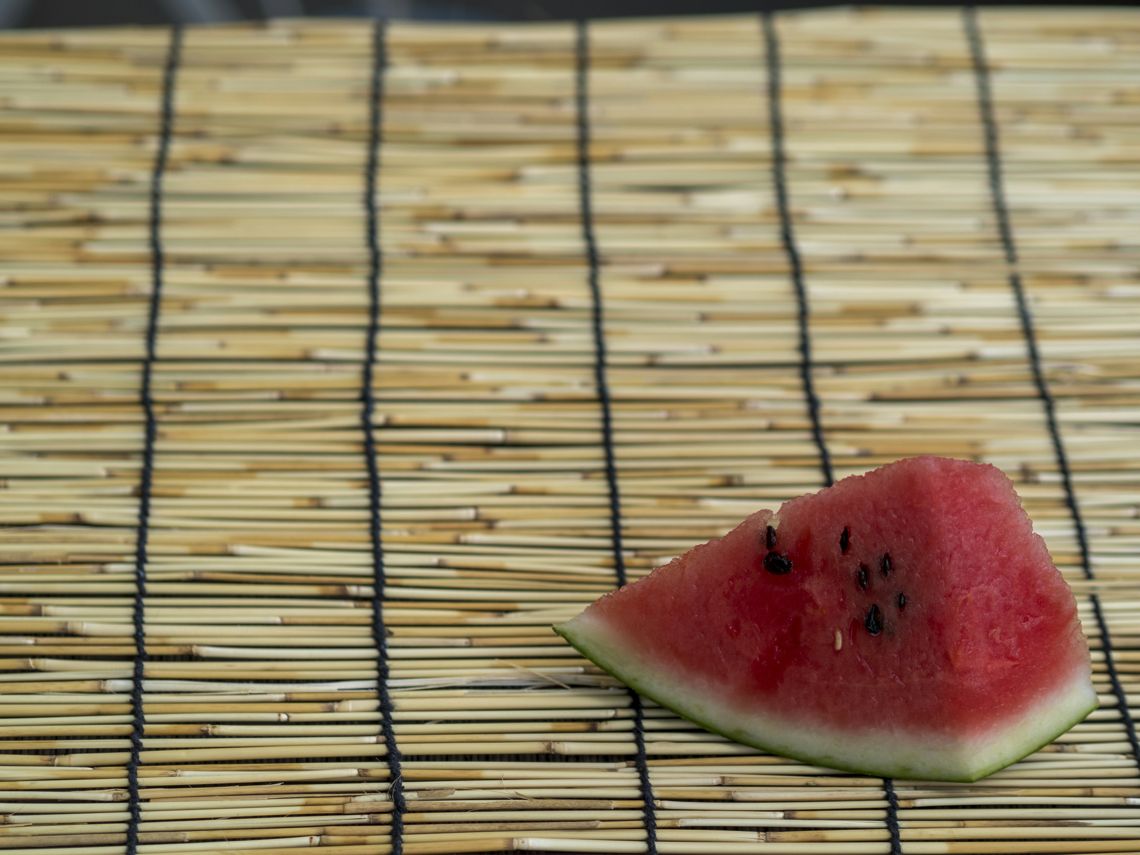 A slice of watermelon rests on a bamboo mat