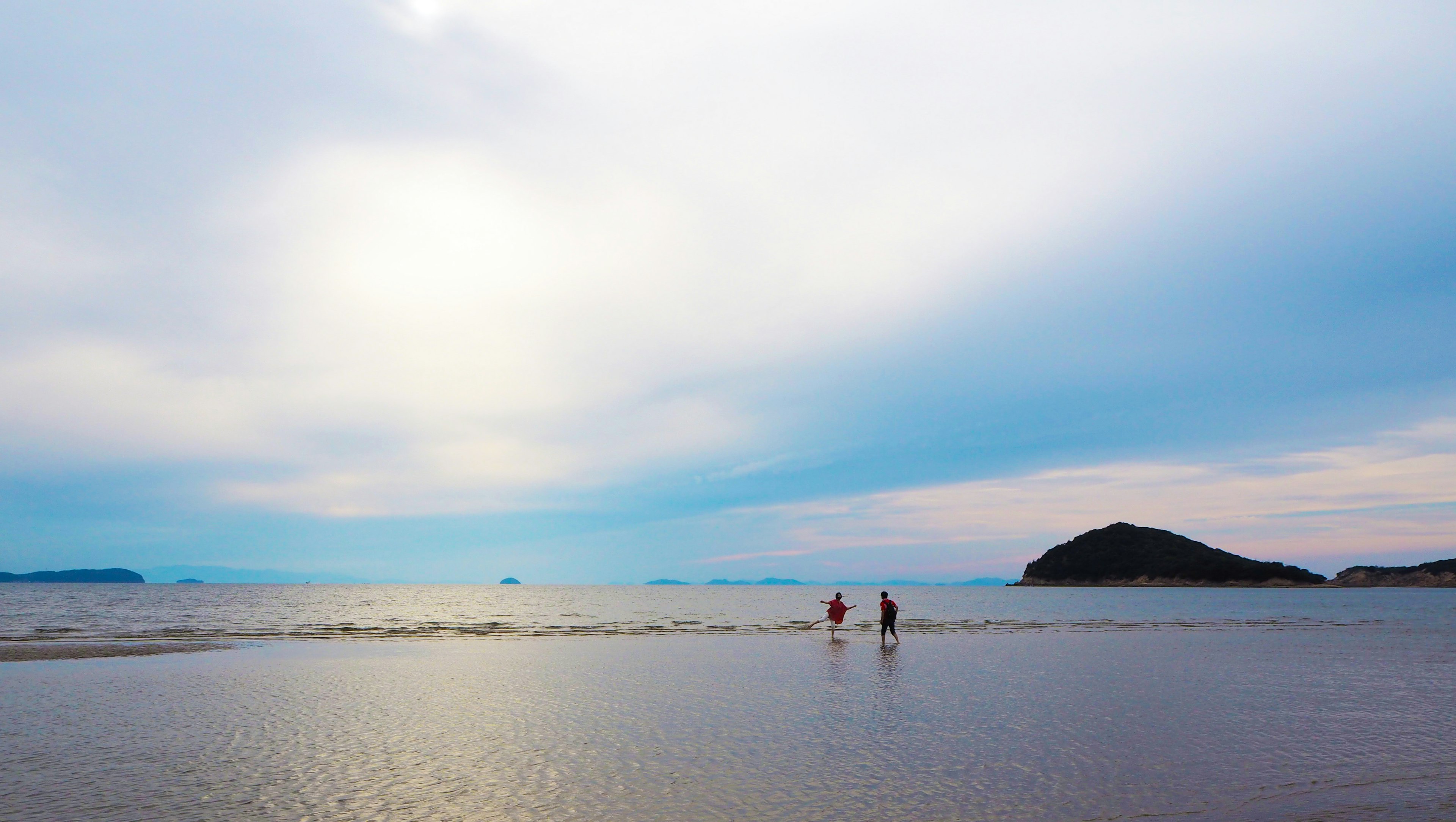 ผู้คนเดินเล่นบนชายหาดที่เงียบสงบใต้ท้องฟ้าสีฟ้า