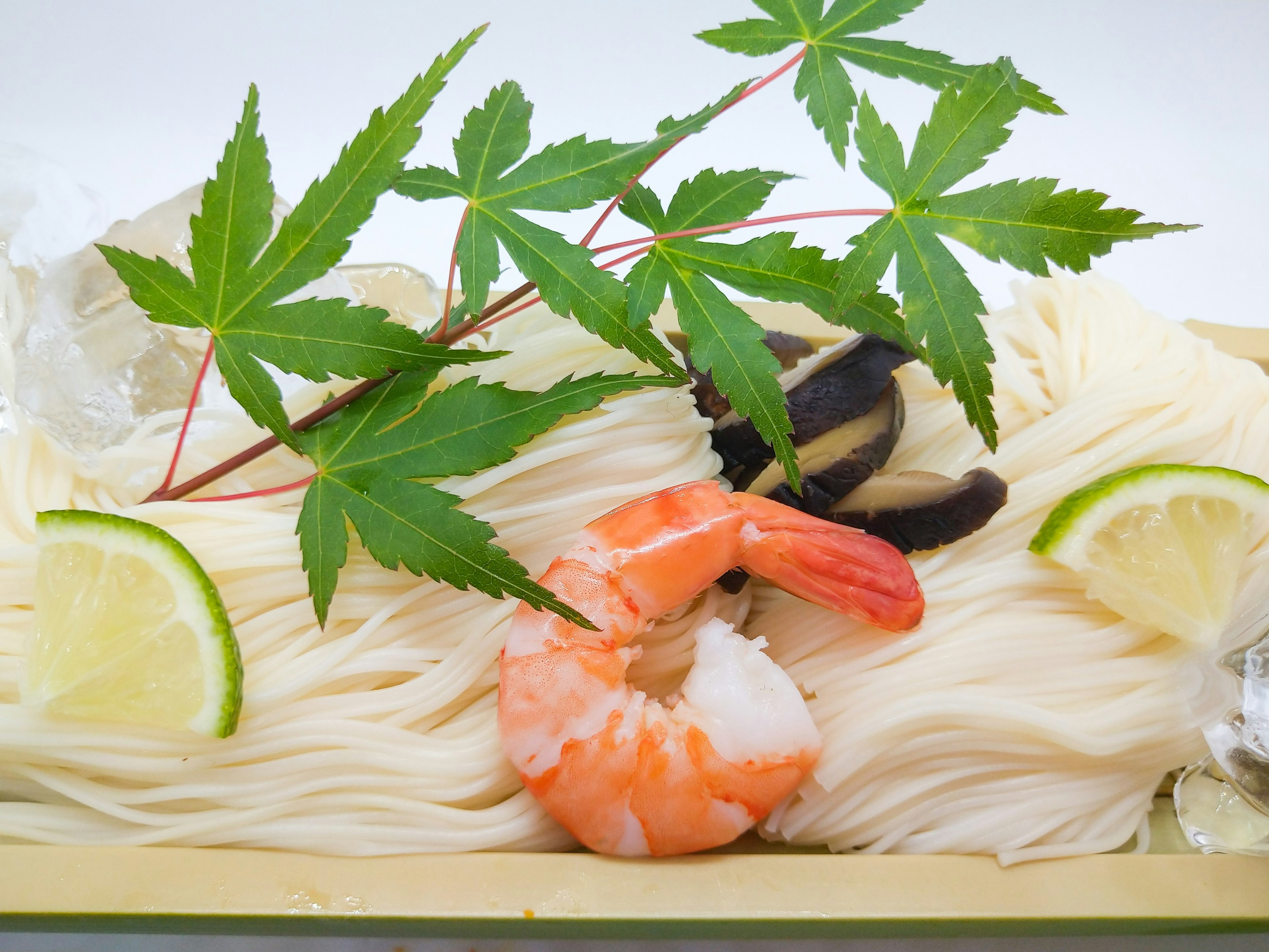 Cold somen noodles garnished with fresh shrimp lime slices and green leaves