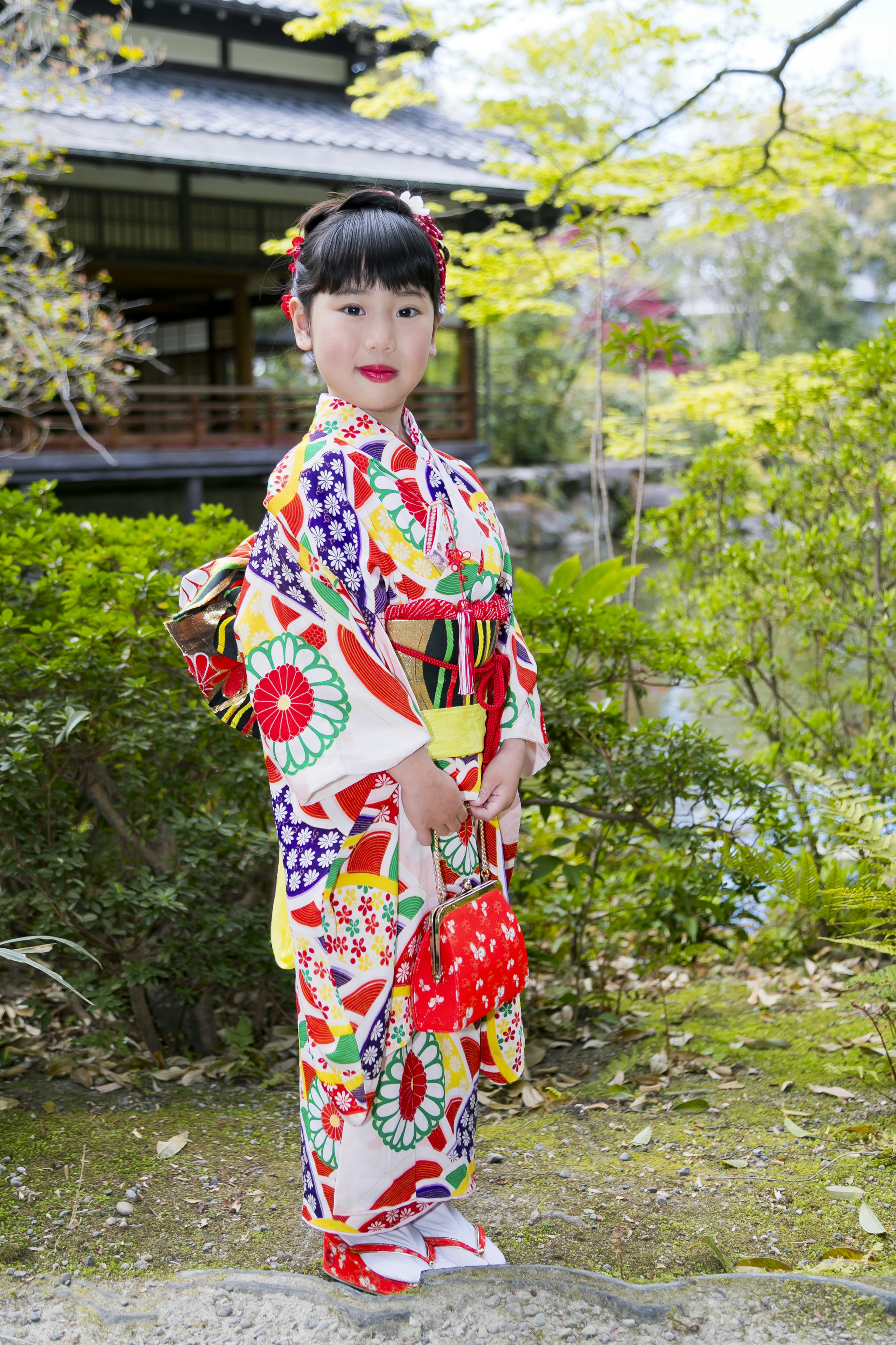 Seorang gadis muda mengenakan kimono berwarna-warni berdiri di taman