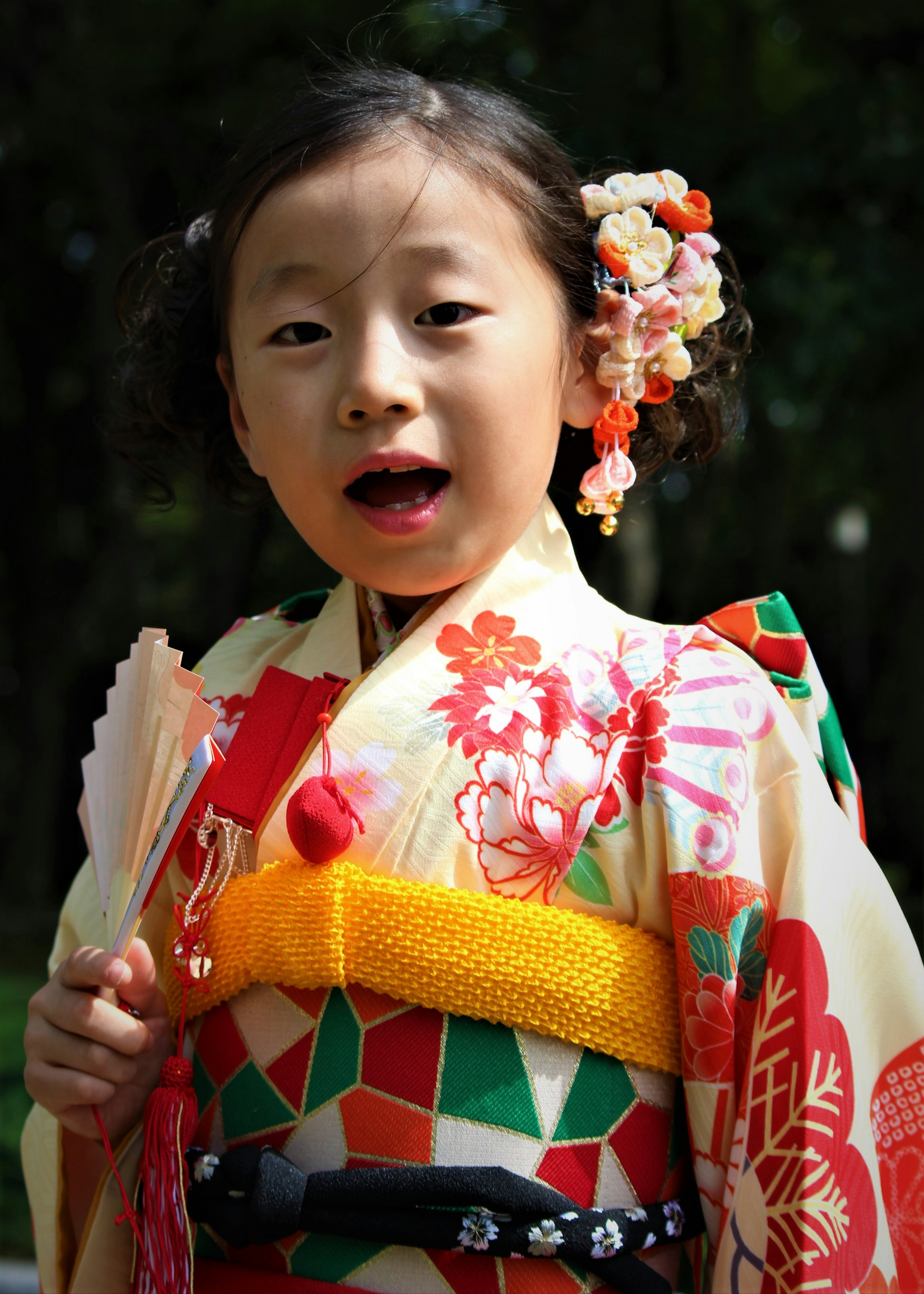 Una niña con un kimono colorido sonríe mientras sostiene un abanico