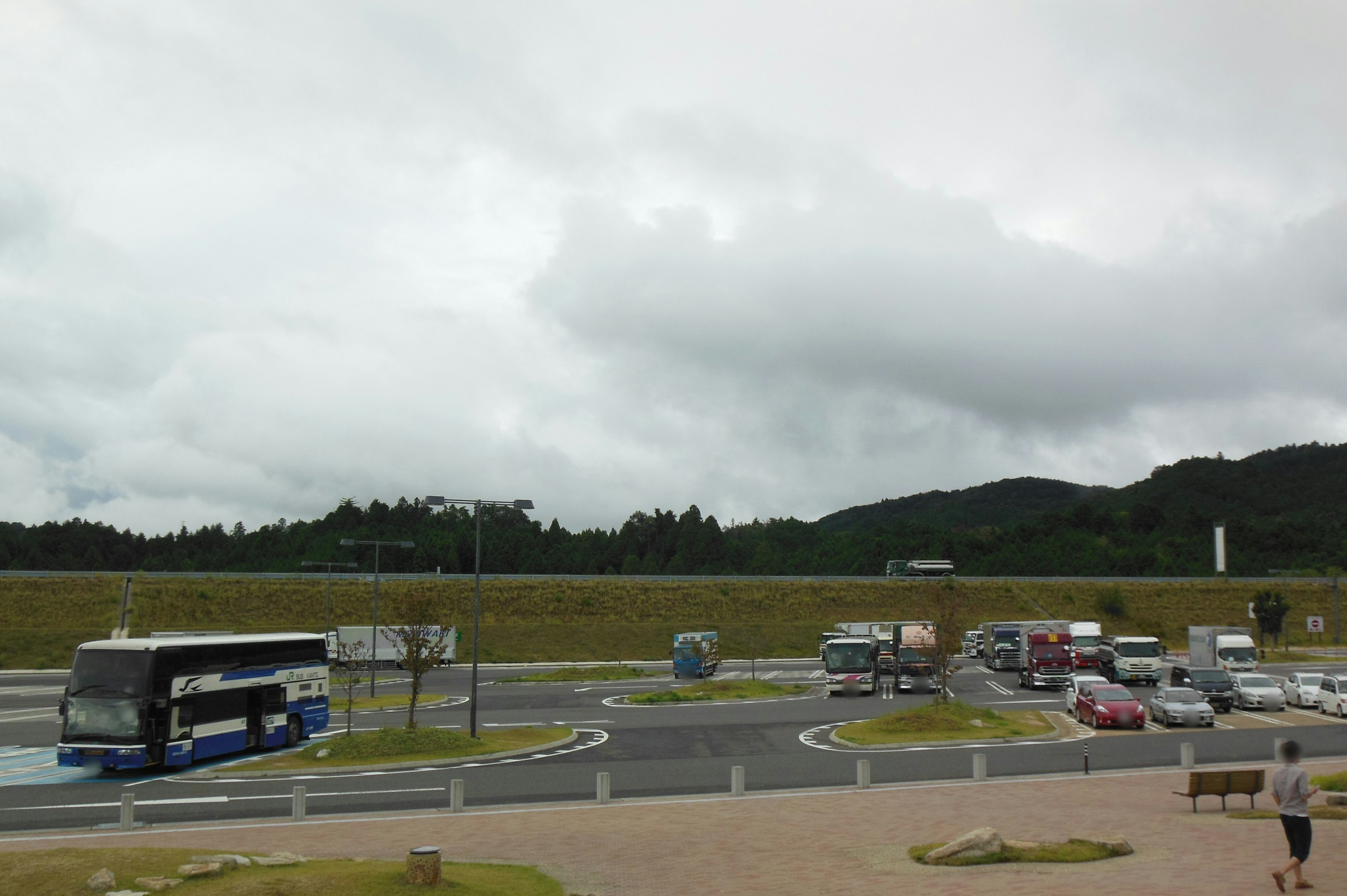 Vue d'un rond-point avec un bus et des voitures sous un ciel nuageux collines vertes en arrière-plan