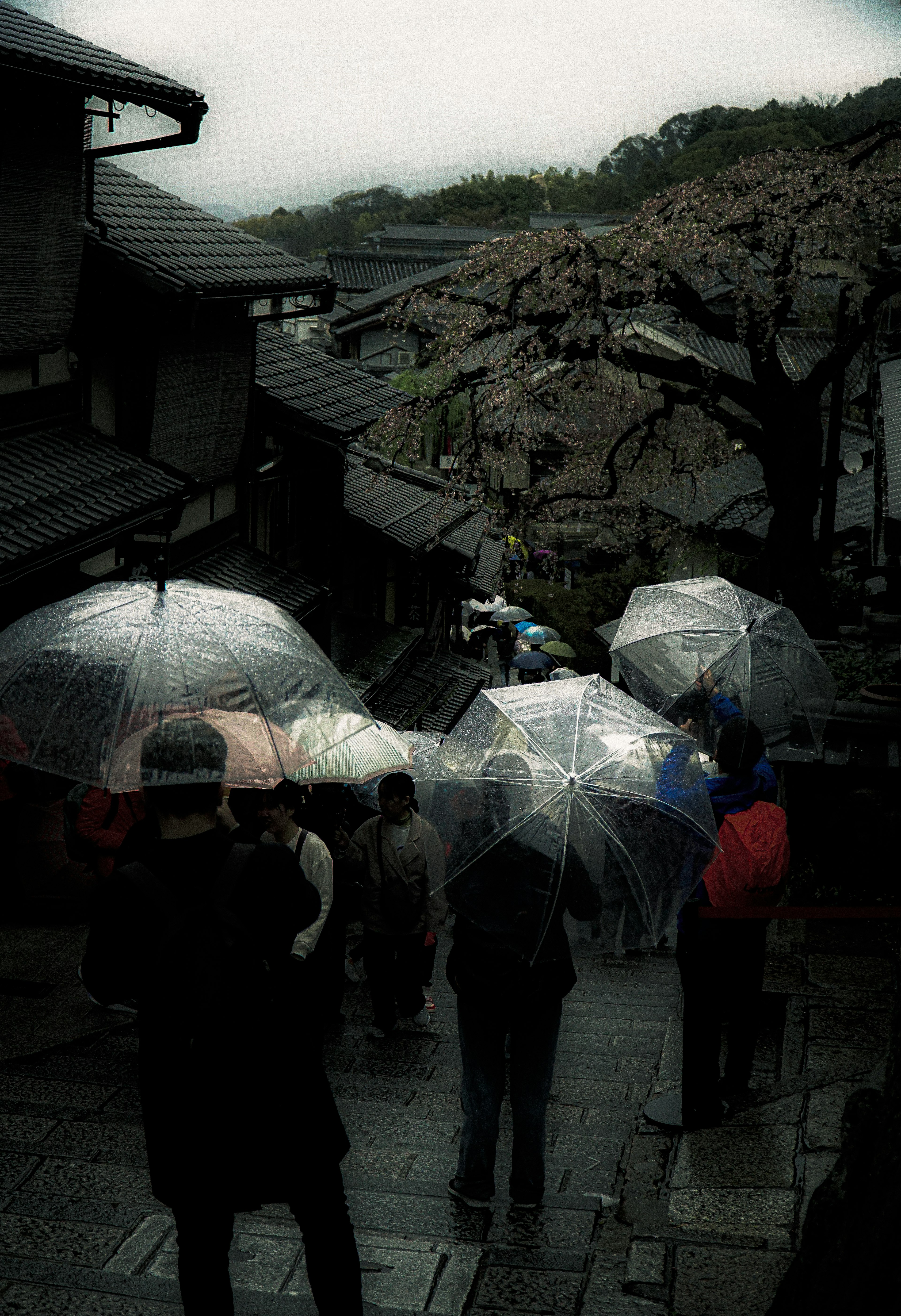 Des gens avec des parapluies dans une scène pluvieuse avec des bâtiments anciens et un paysage rocheux