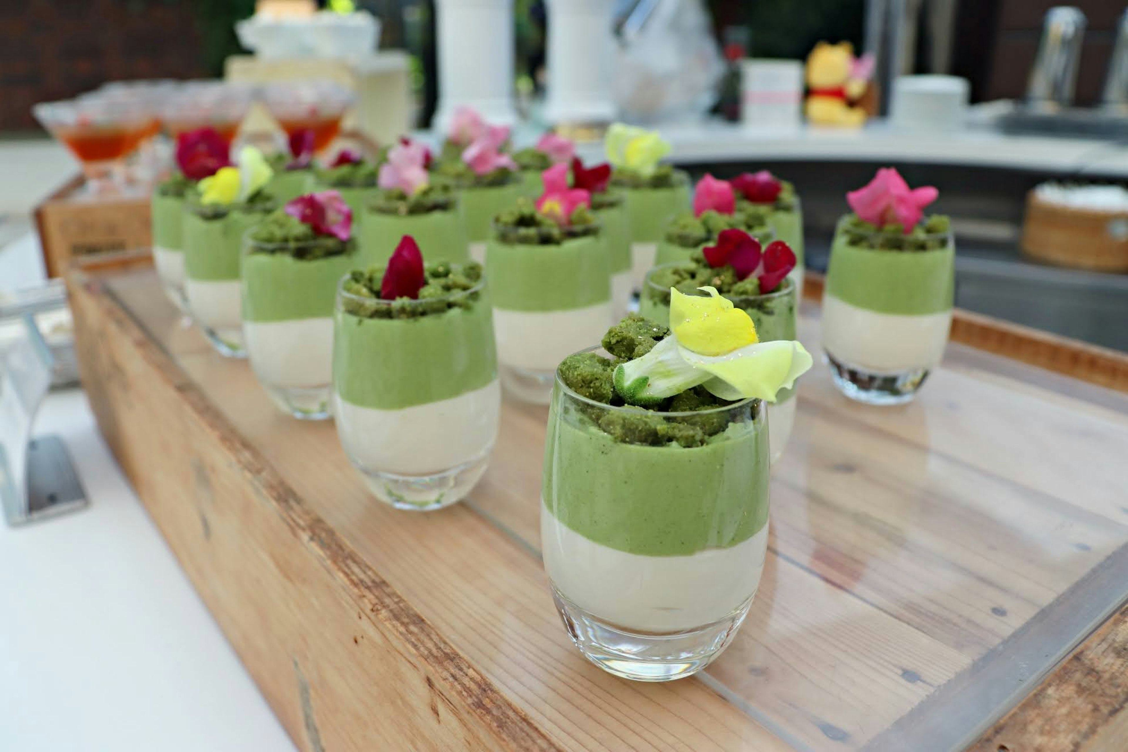 Cangkir pencuci mulut dengan mousse matcha berlapis dan krim, dihiasi dengan bunga yang dapat dimakan