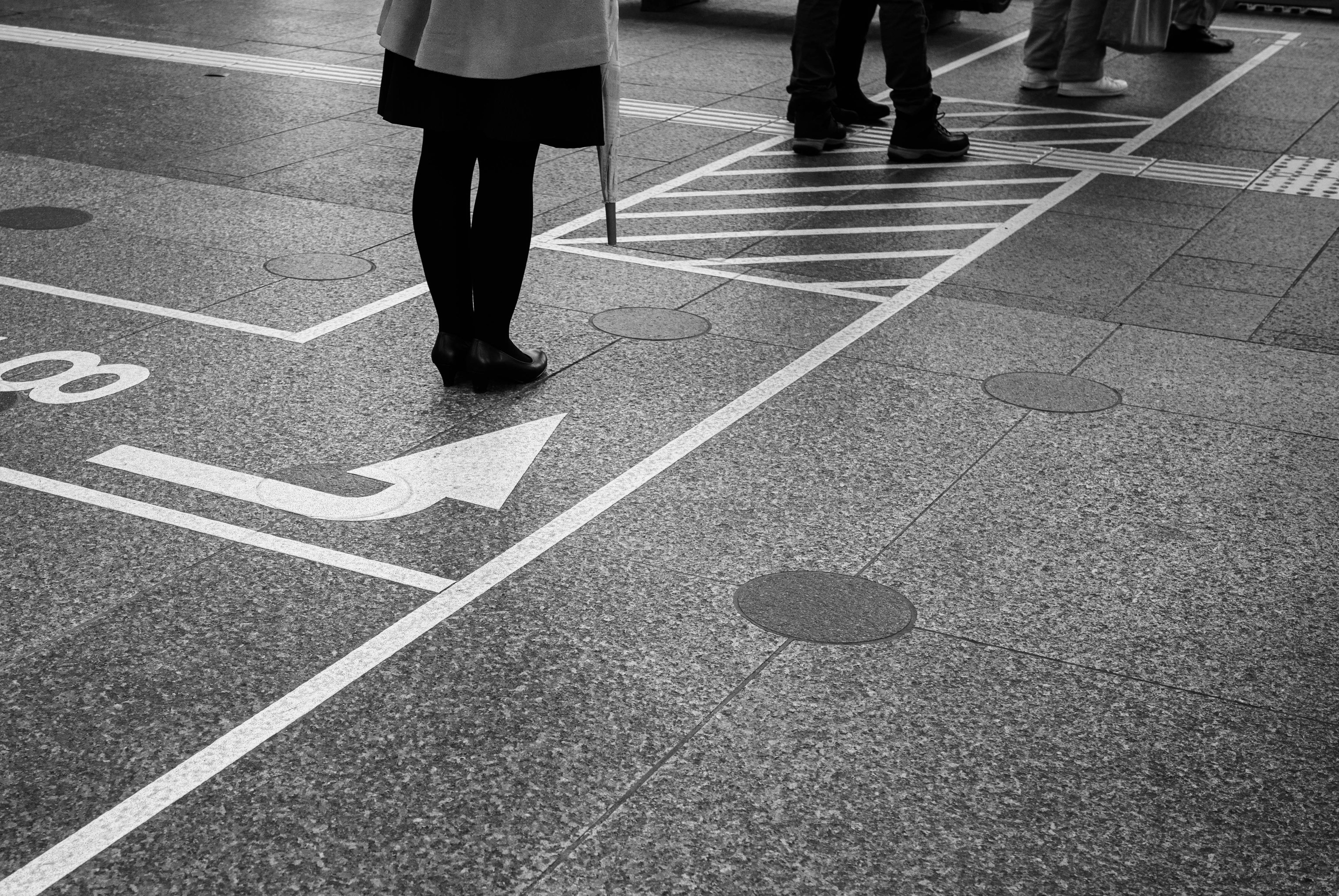 Seorang wanita dengan payung berdiri di zebra cross dengan tanda arah