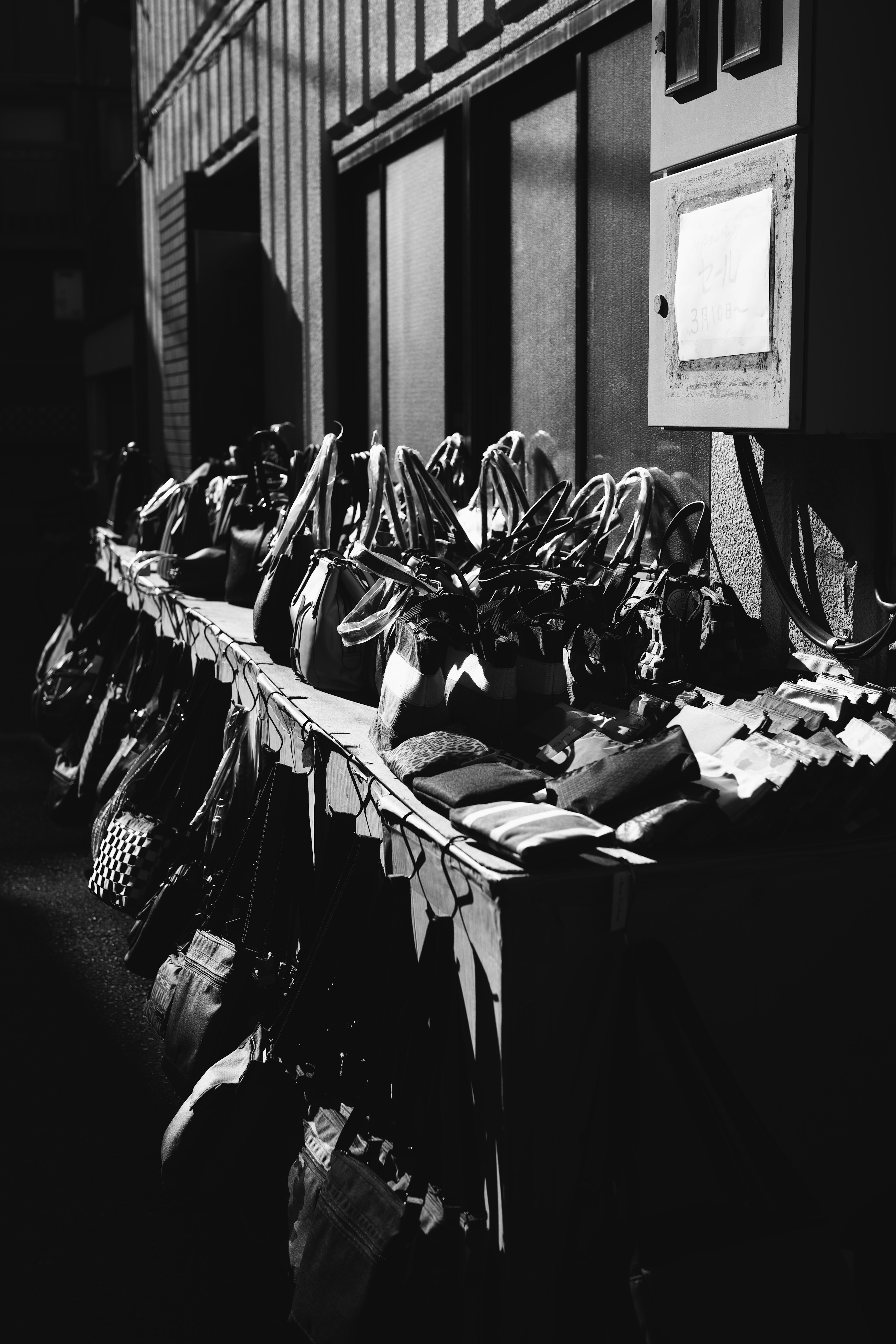 Black and white photograph featuring a row of various bags and items