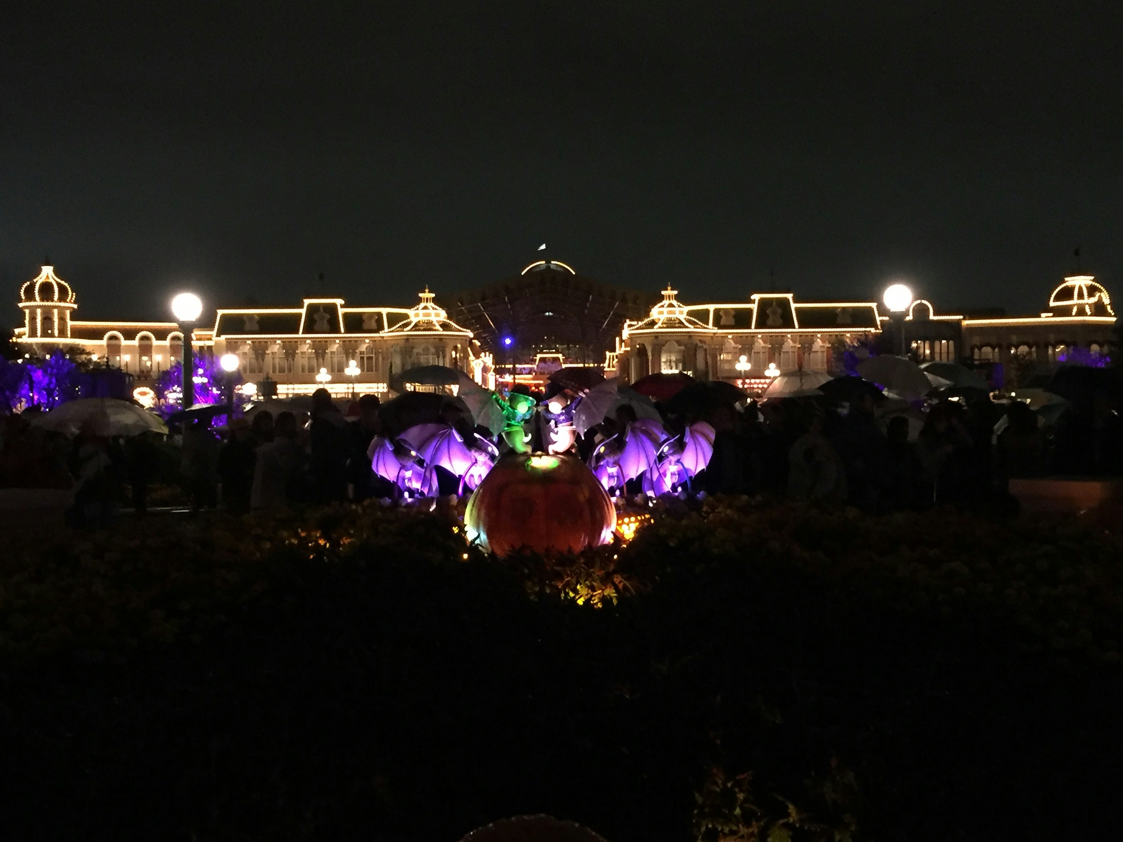 Illuminated theme park buildings at night with colorful Halloween decorations