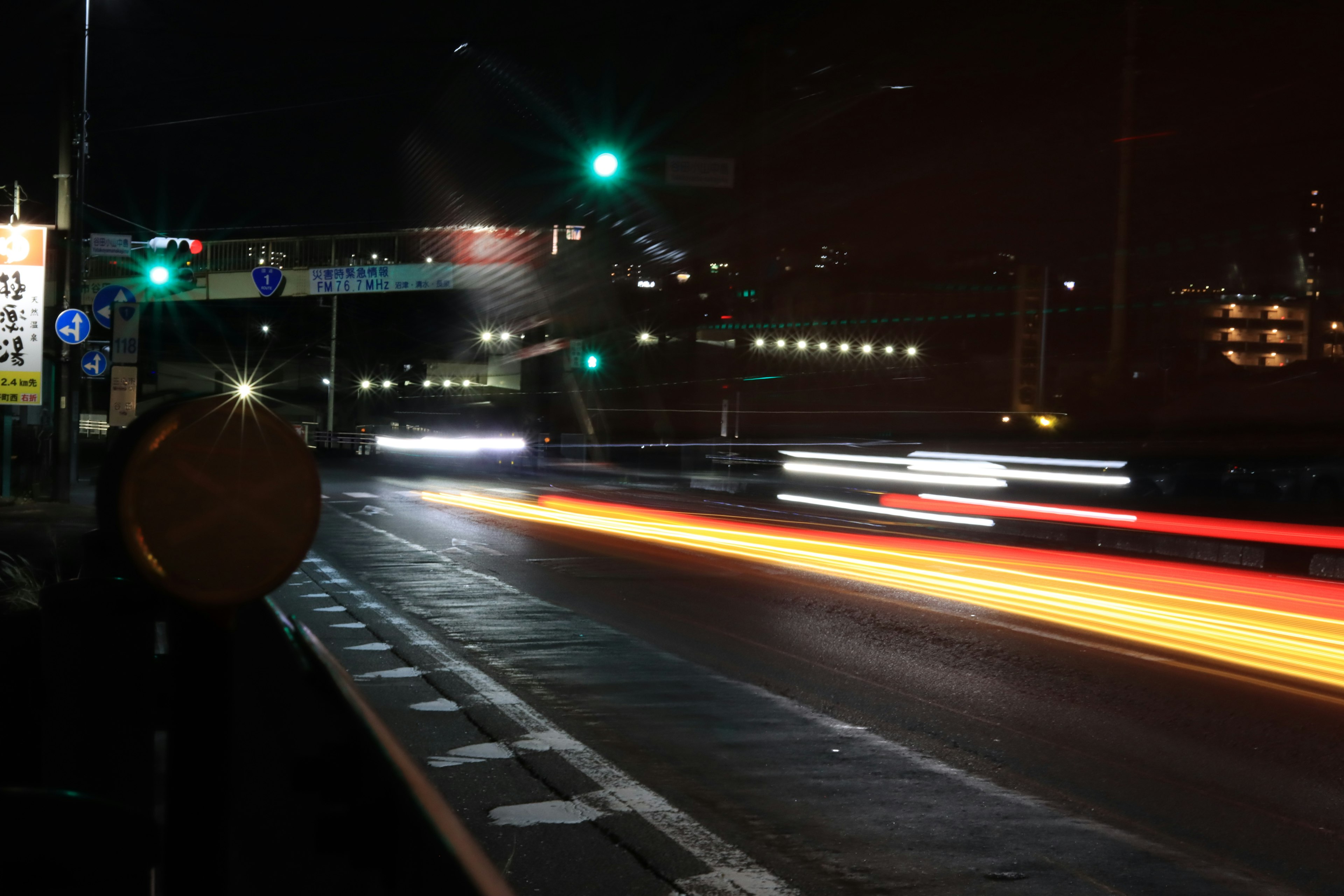 Autolichter blitzen auf einer dunklen Straße mit einer grünen Ampel