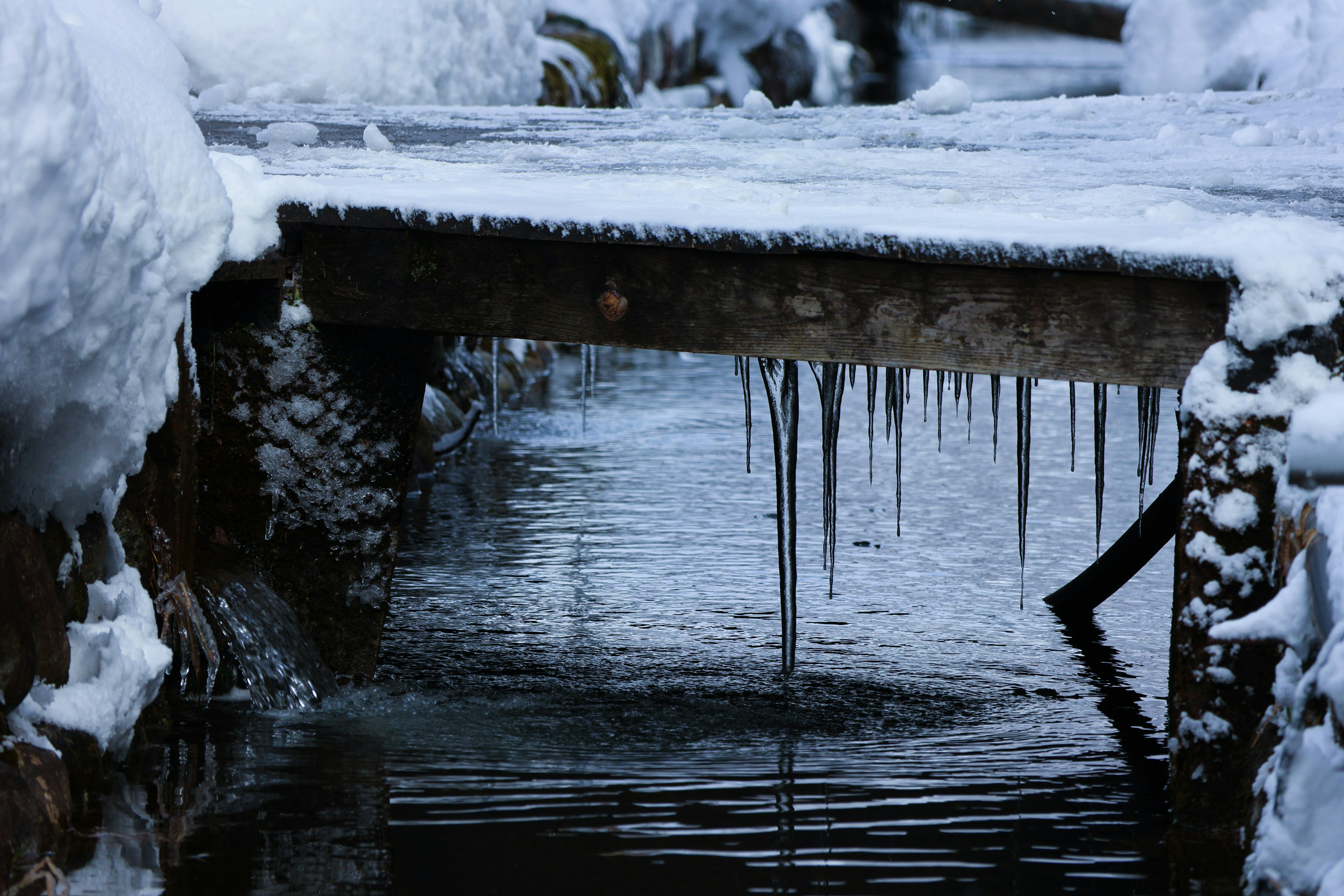 Cây cầu phủ tuyết với icicles trên bề mặt nước yên tĩnh