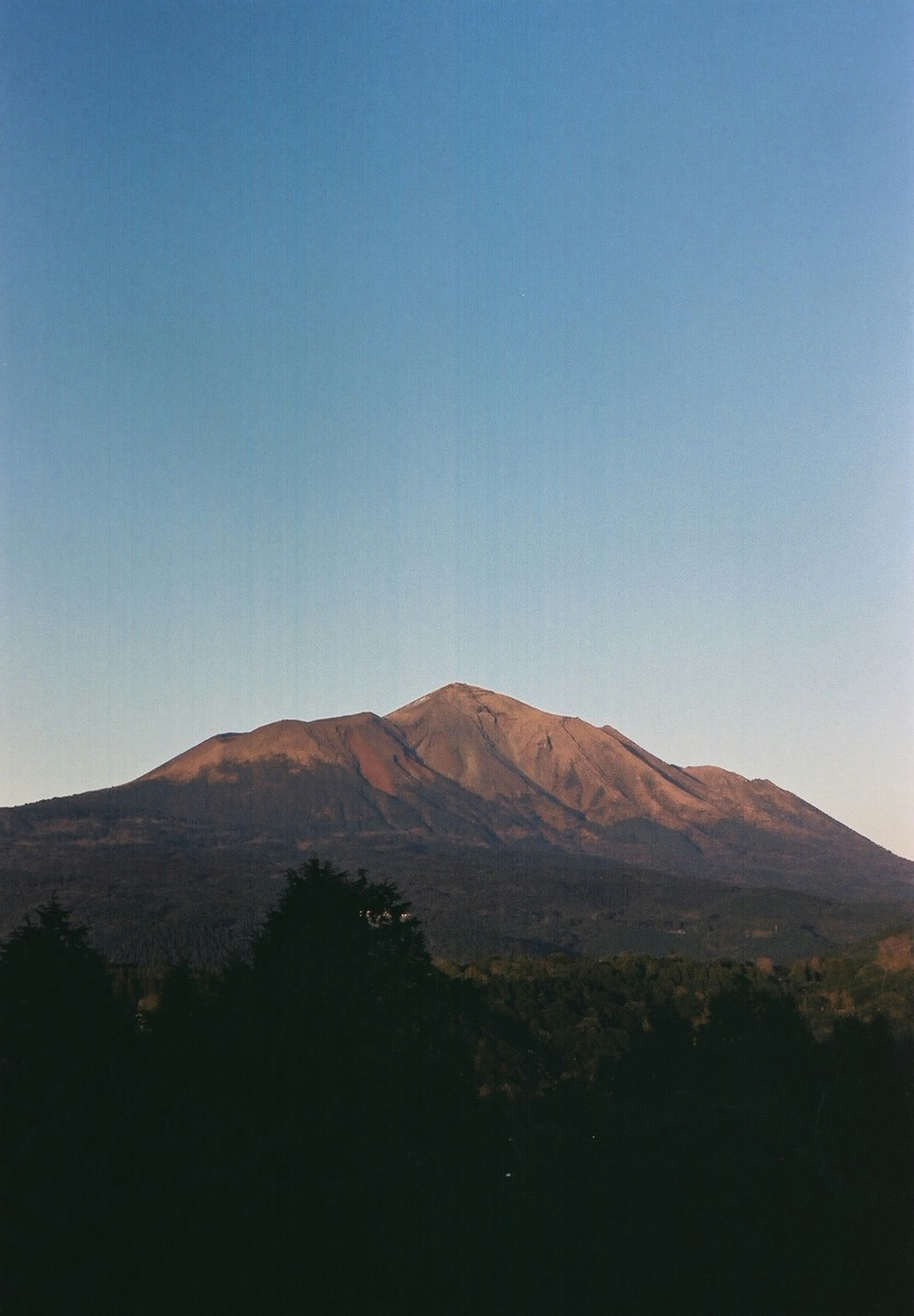 Un paisaje montañoso sereno con un brillo de atardecer contra un cielo azul