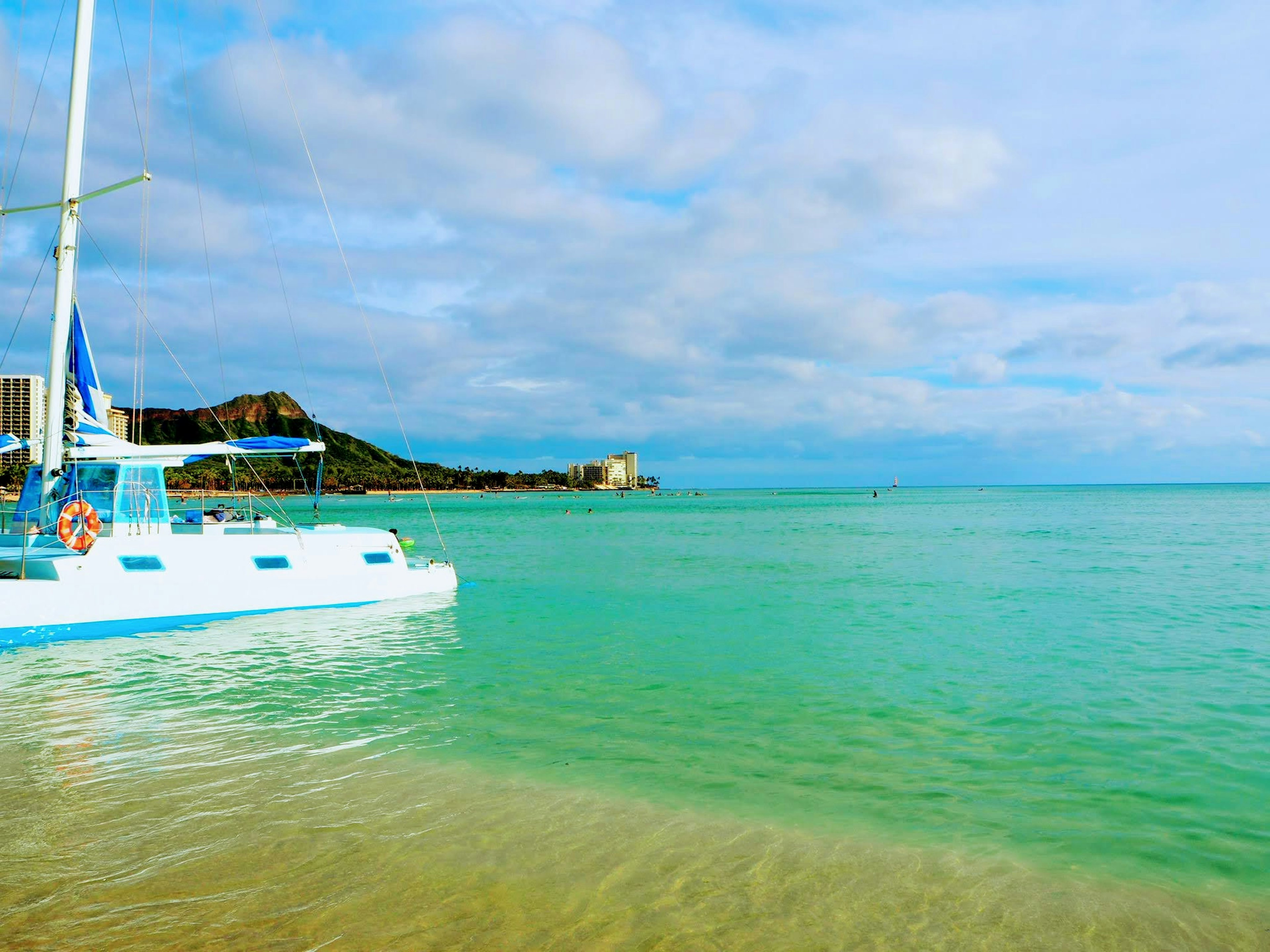 Escena de playa con un océano azul y un velero blanco