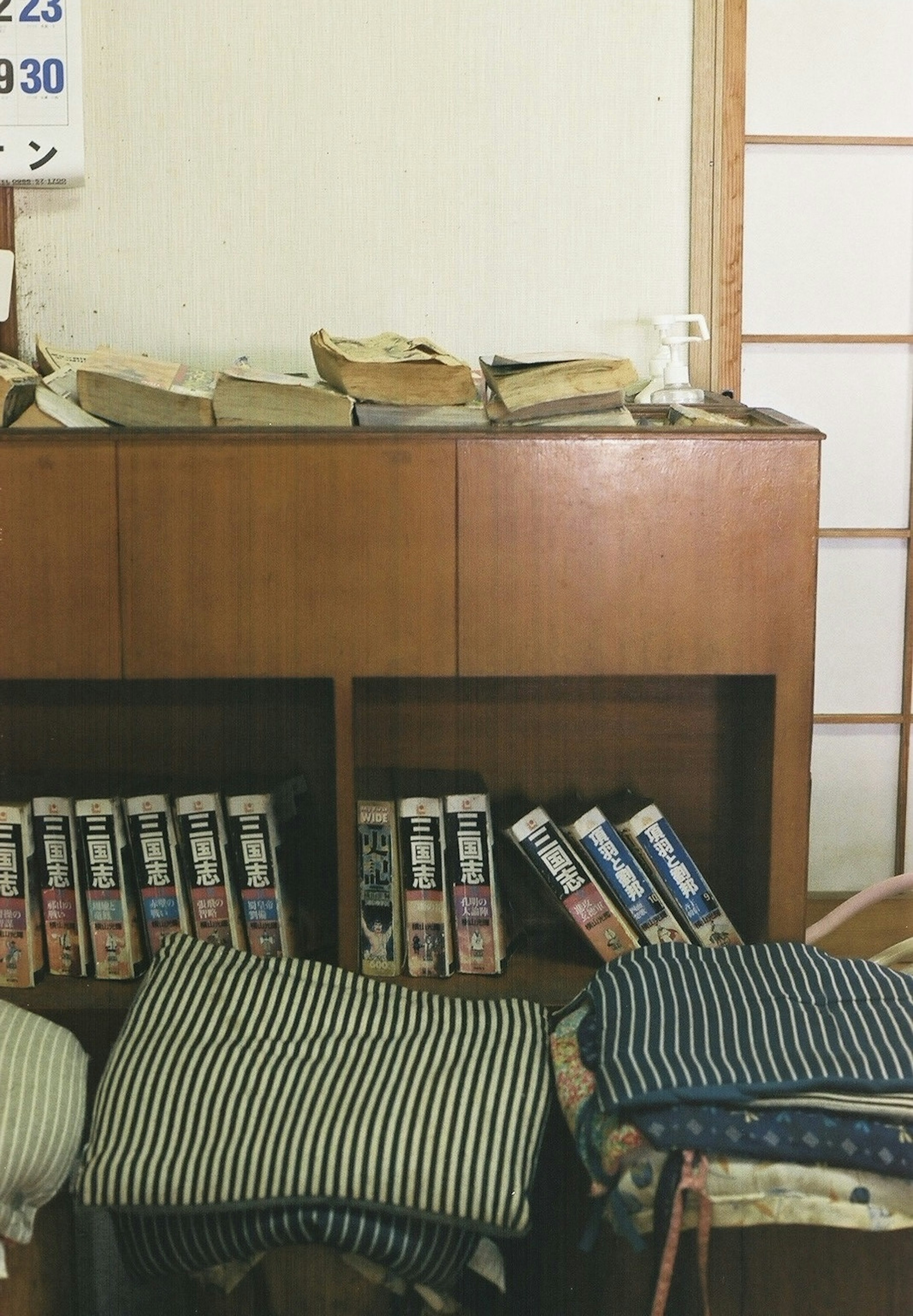 Interior of a room with a wooden cabinet stacked with books and striped cushions on the floor