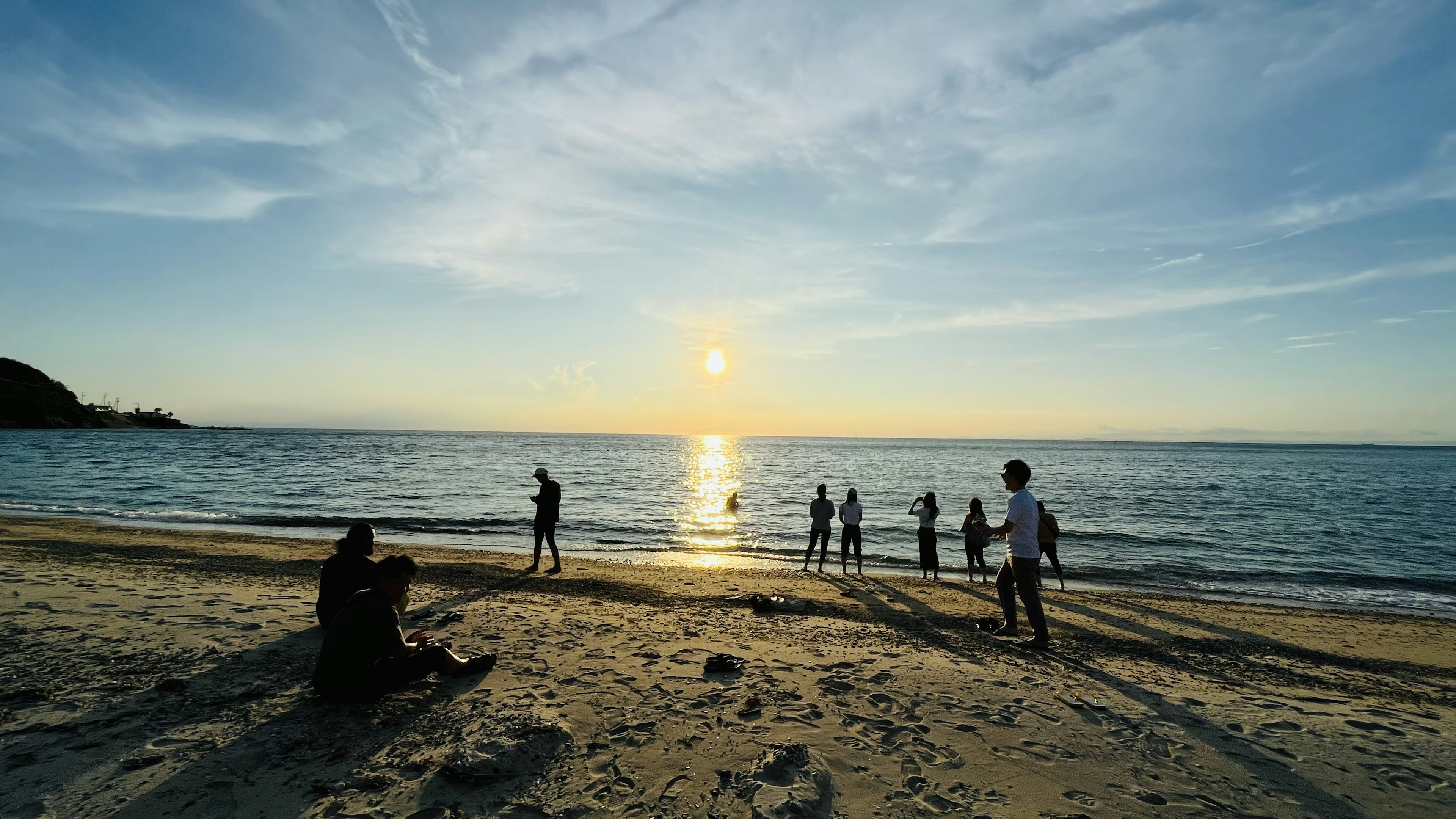 People enjoying a beach at sunset with calm waves and silhouettes