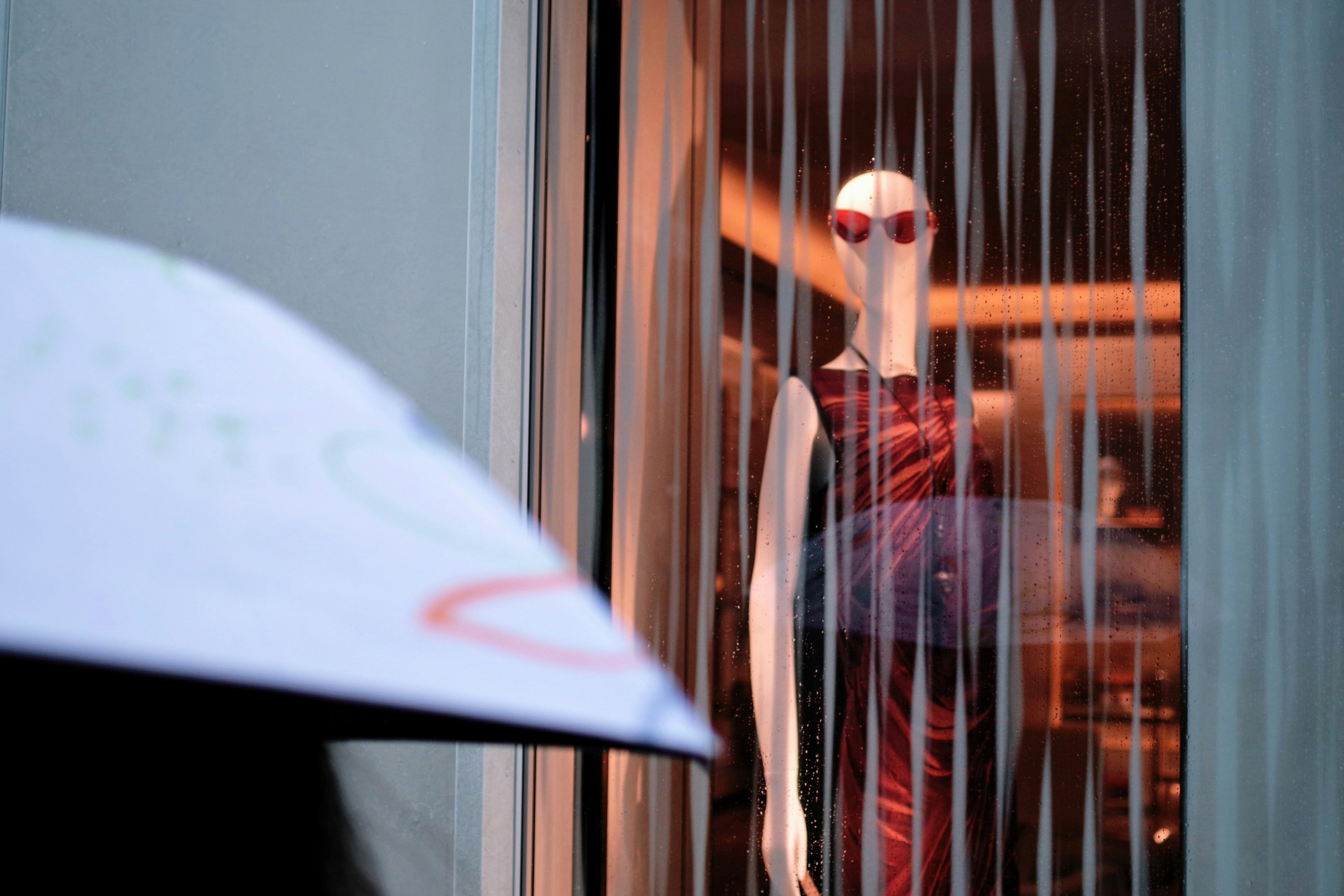 A mannequin in a red dress displayed in a shop window with blurred lighting in the background