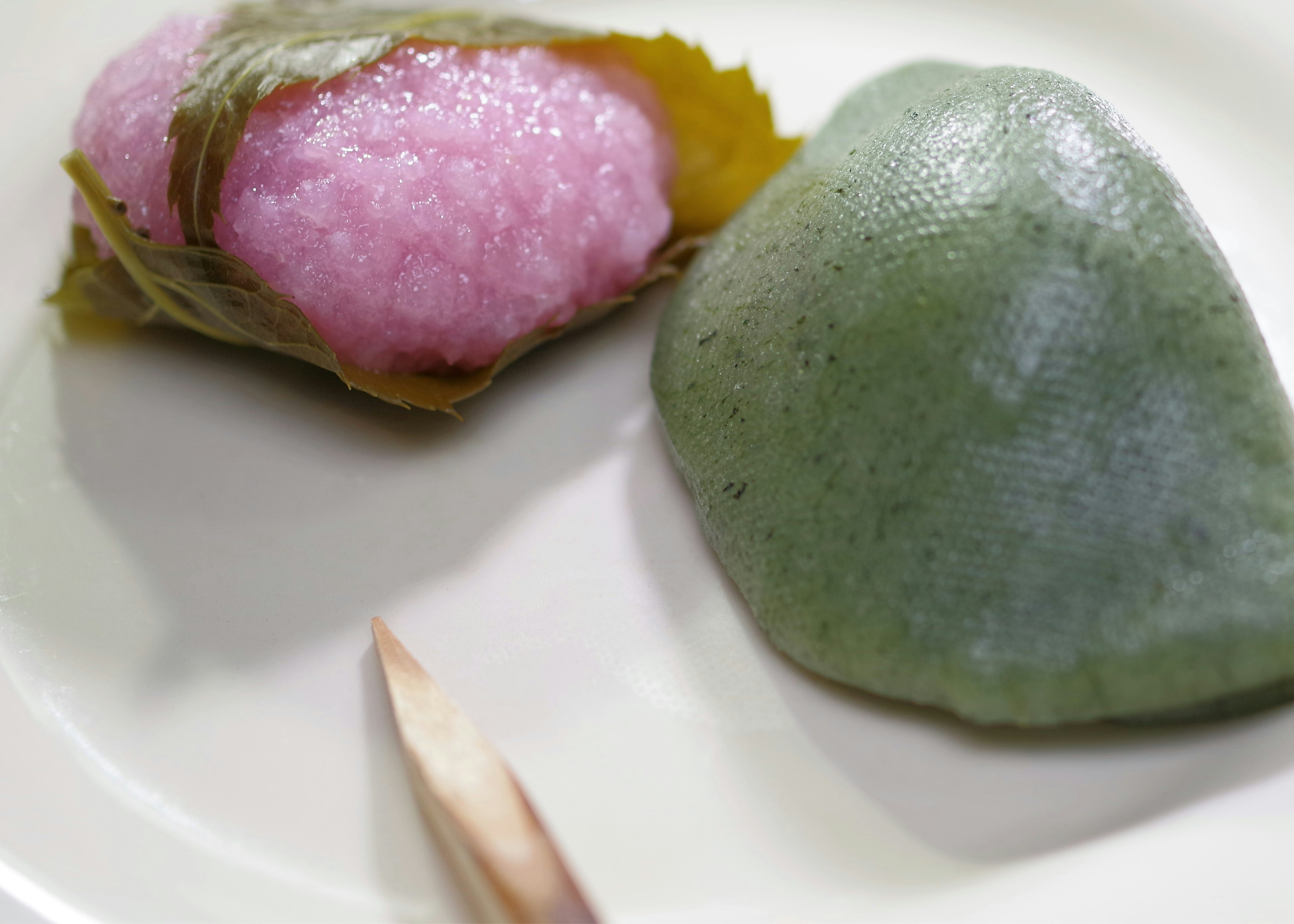 Pink wagashi wrapped in a cherry leaf and green wagashi on a white plate