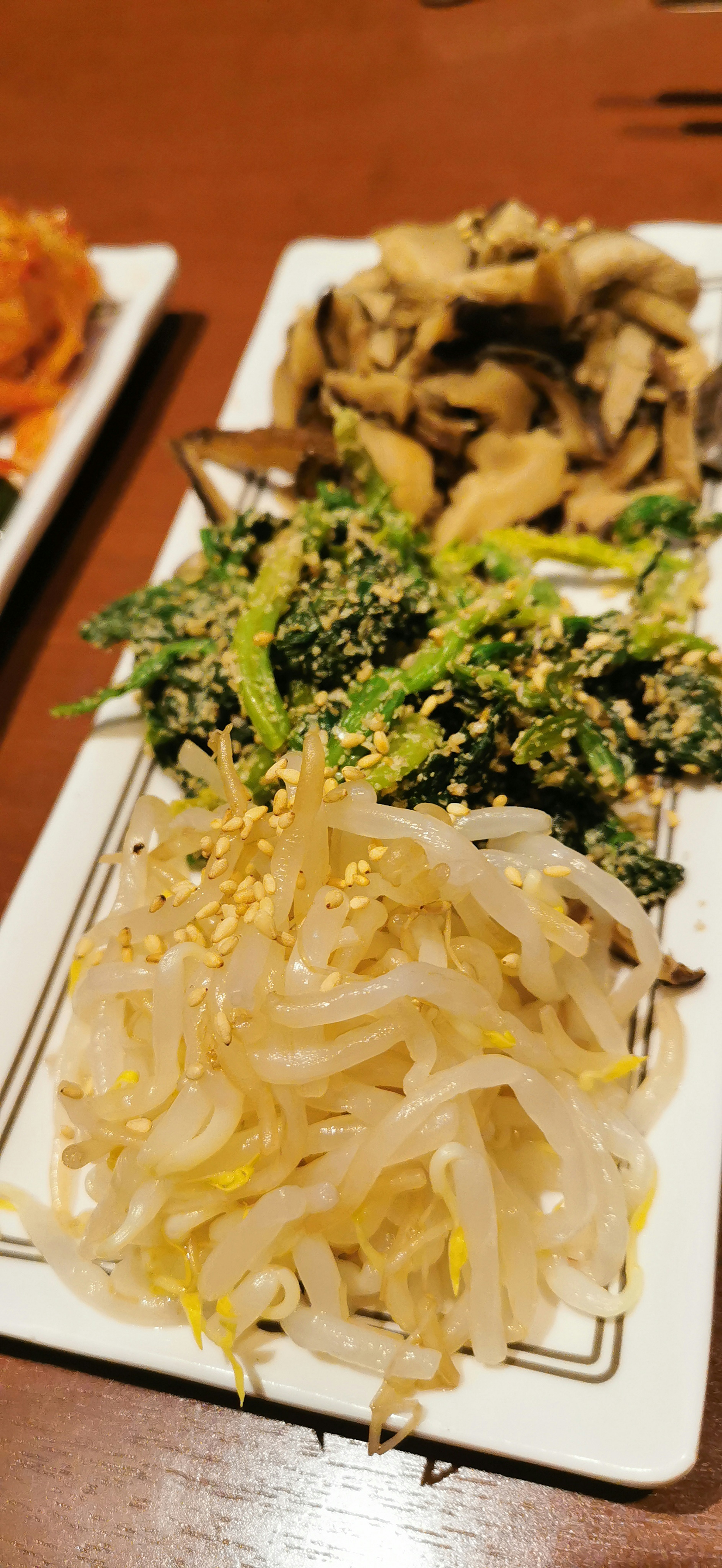 A platter of Korean side dishes featuring bean sprouts, greens, and mushrooms beautifully arranged