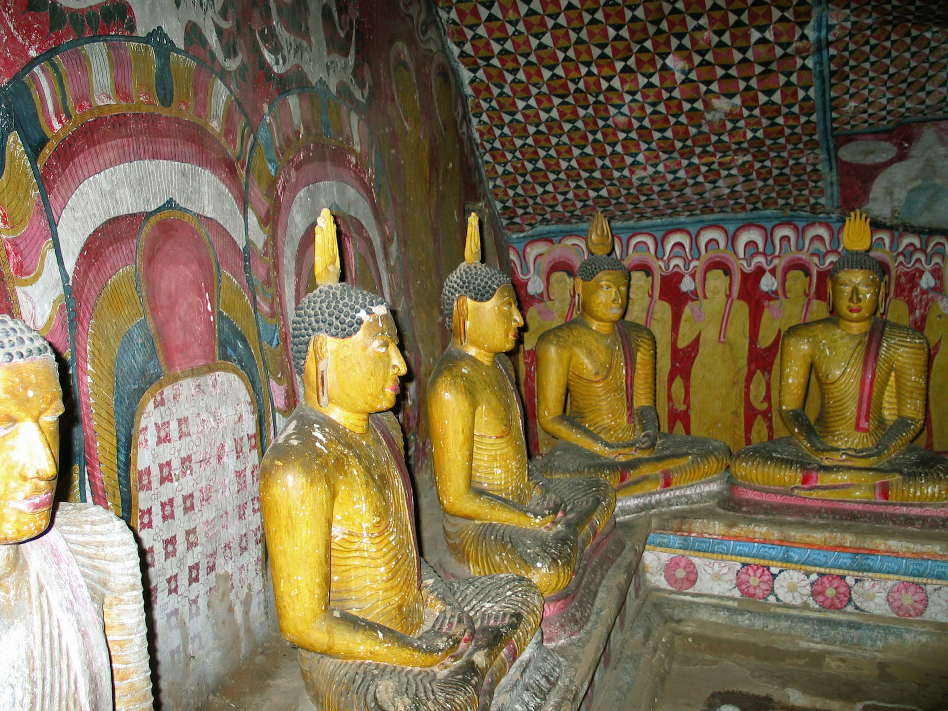 Estatuas de Buda doradas en un templo budista en una cueva con vibrantes pinturas murales