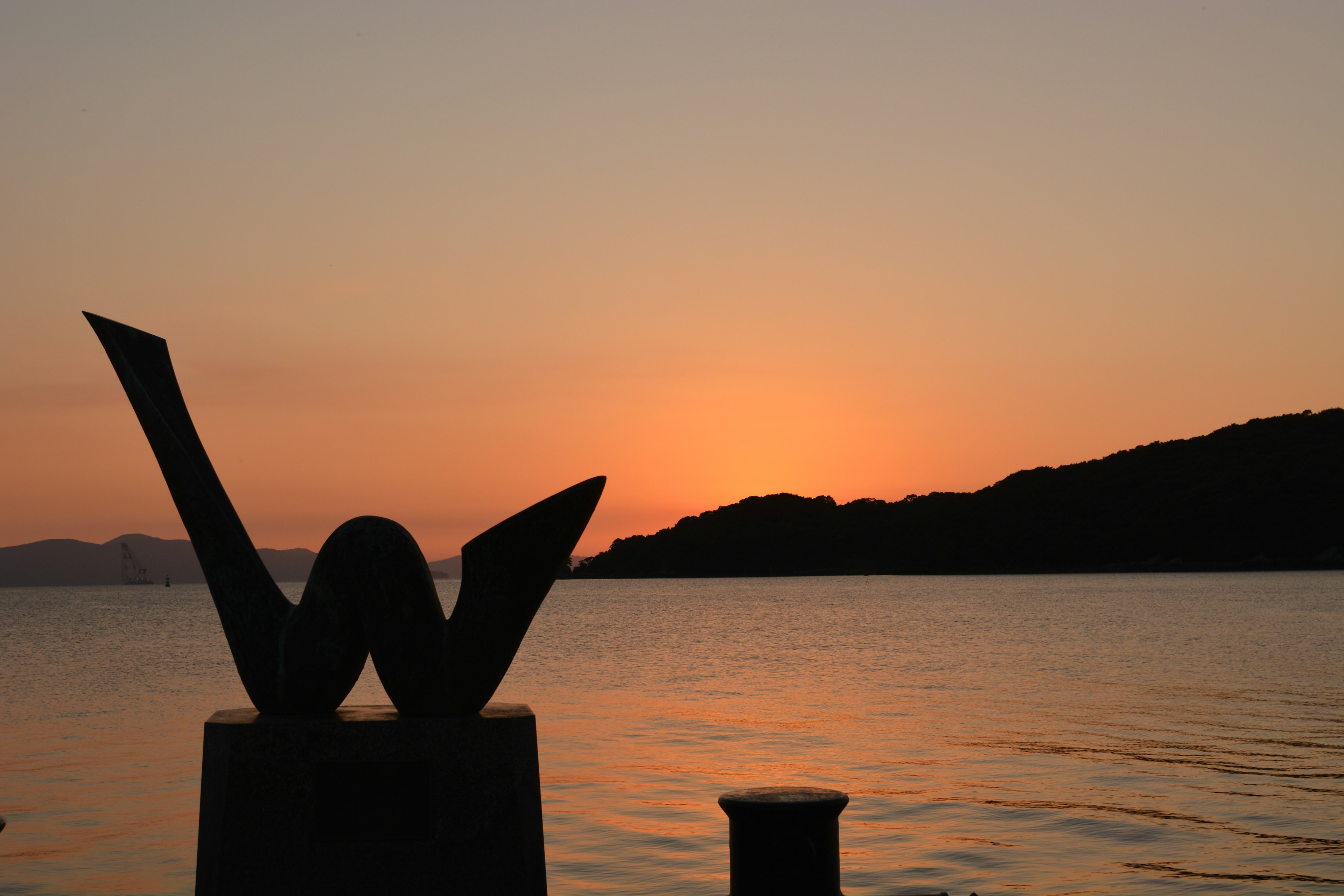 夕日の前に立つ彫刻と静かな水面