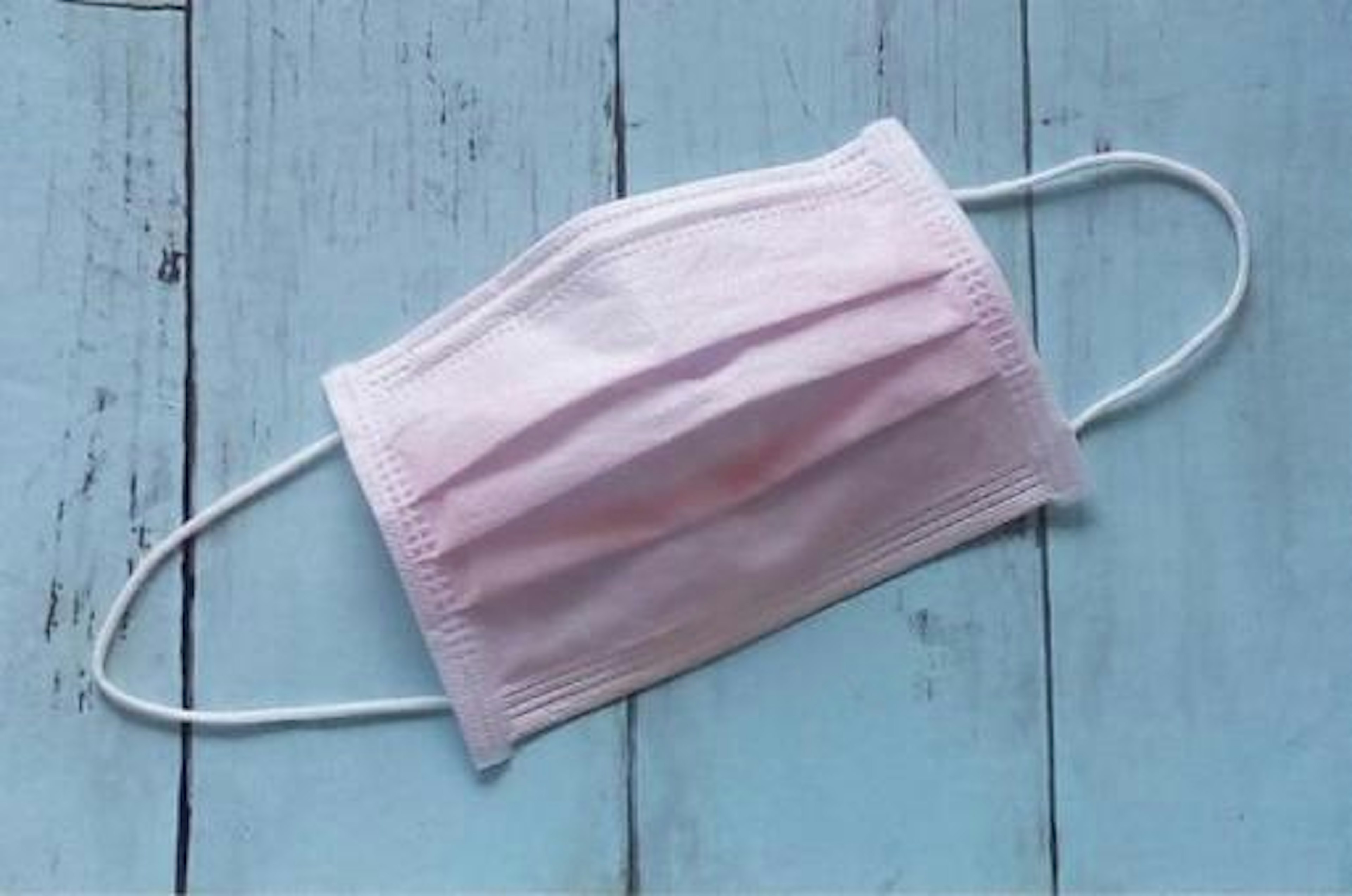 Light pink mask placed on a blue wooden background