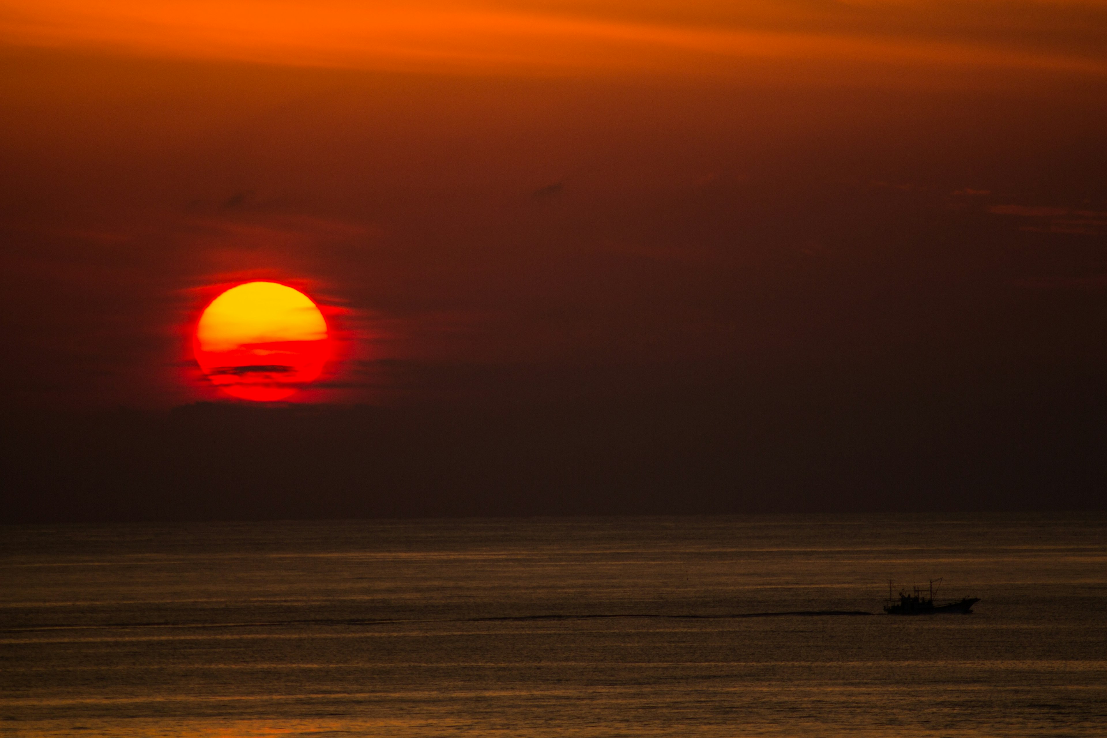 オレンジ色の夕日が海に沈むシーン 船が遠くに見える