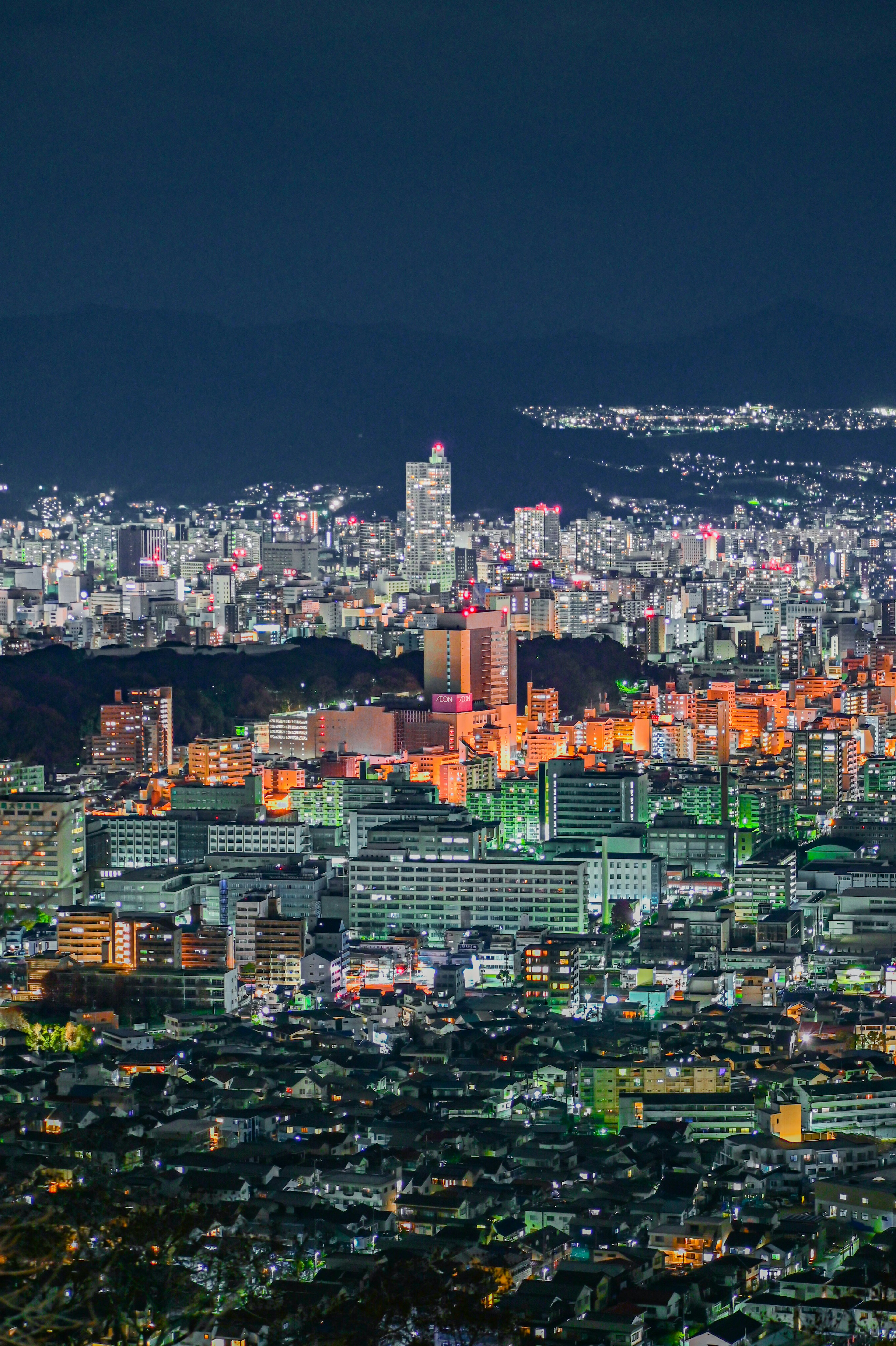 Vista notturna di un skyline urbano con edifici luminosi e silhouette di montagne