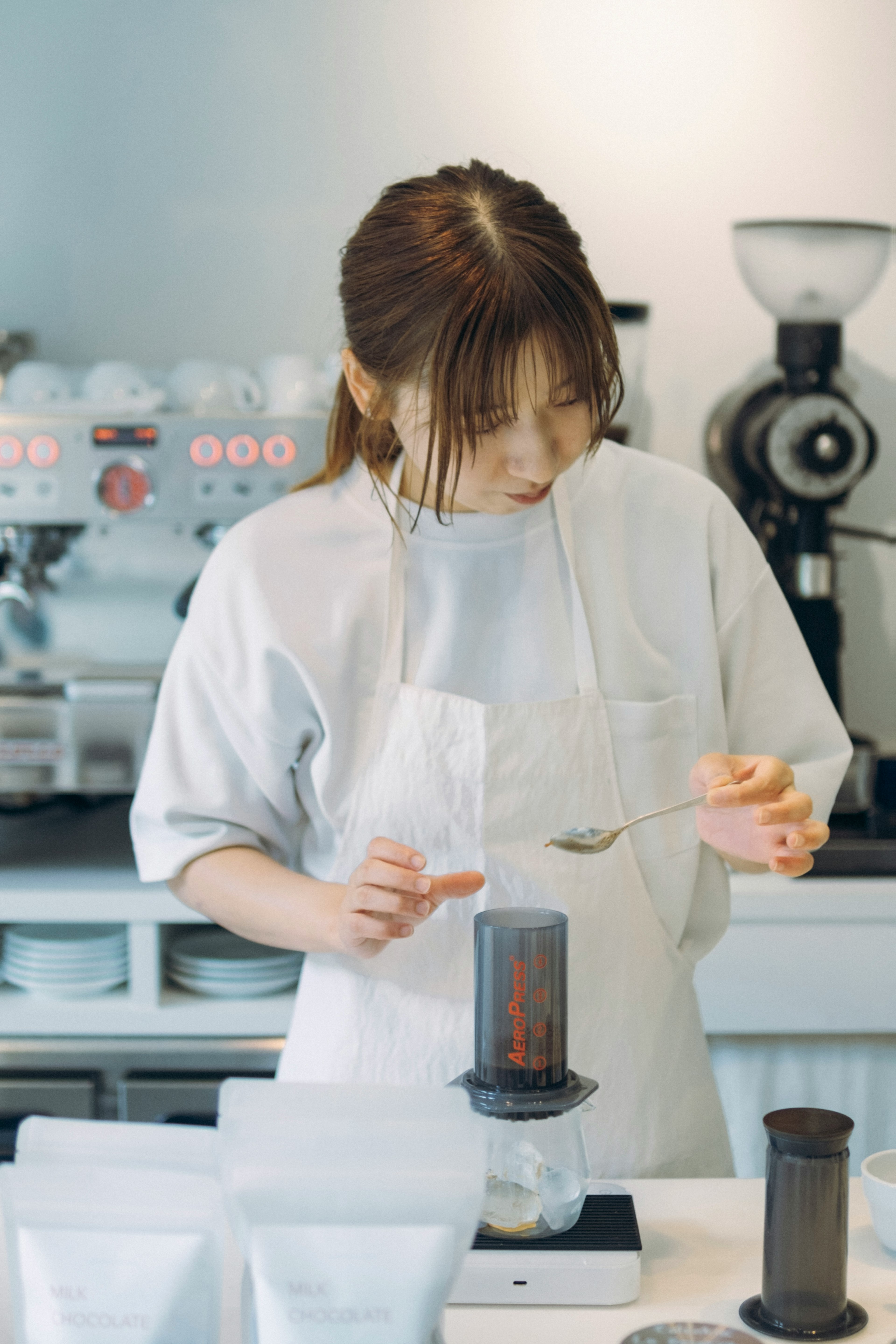 カフェでコーヒーを淹れる女性 バリスタのエプロンを着用 コーヒー器具とパッケージが並ぶ