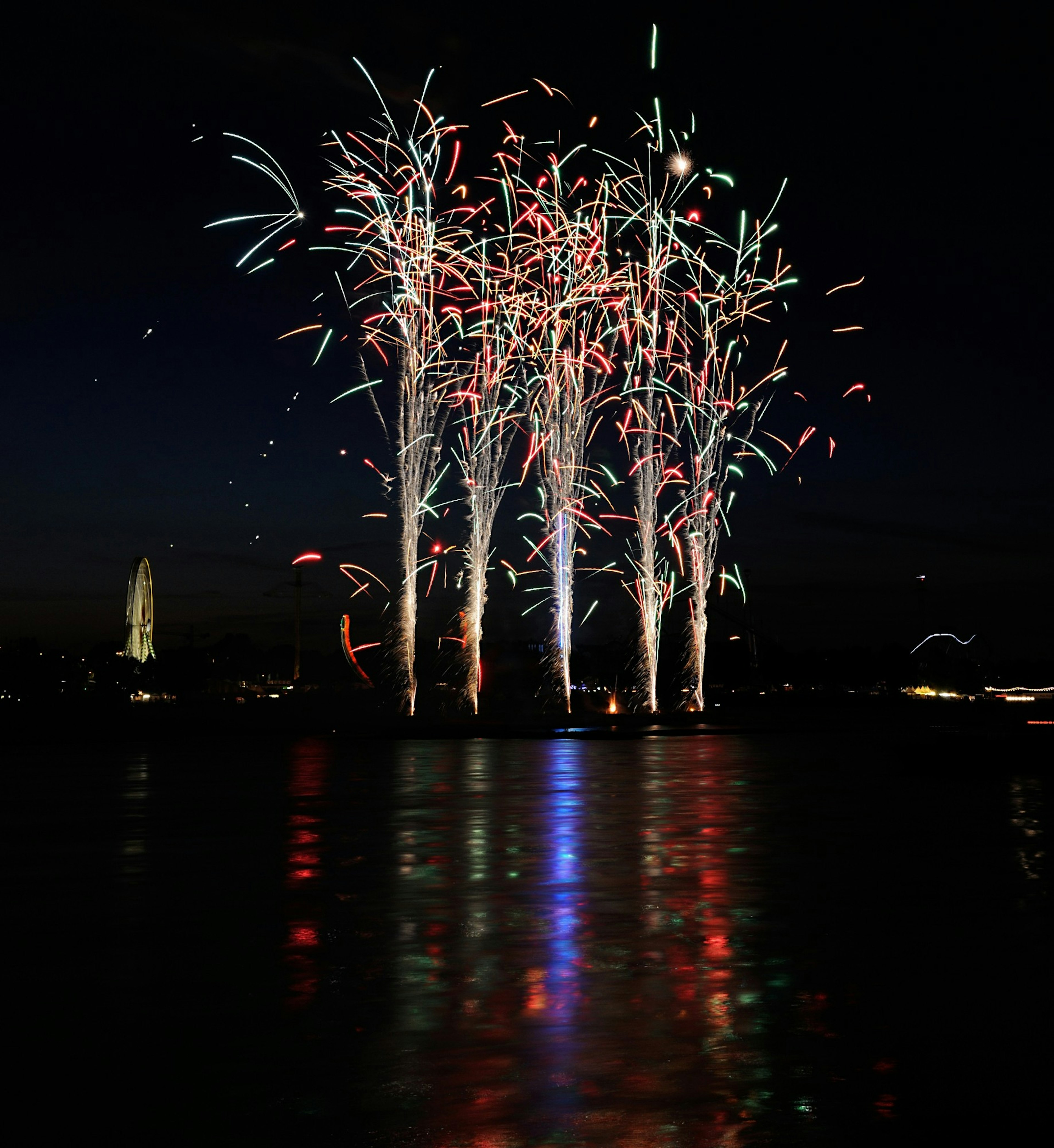 Spettacolo di fuochi d'artificio colorati sopra l'acqua di notte che si riflettono sulla superficie