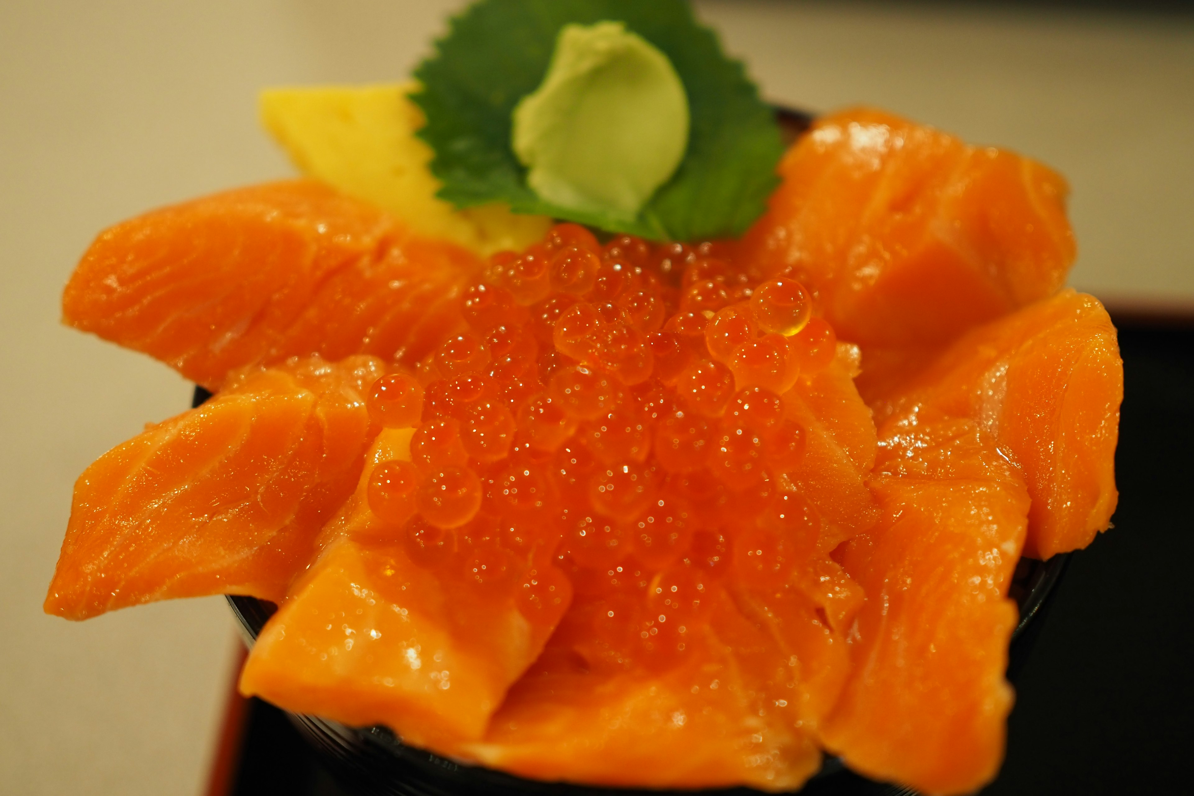 Bowl of salmon sashimi topped with salmon roe wasabi and shiso leaf