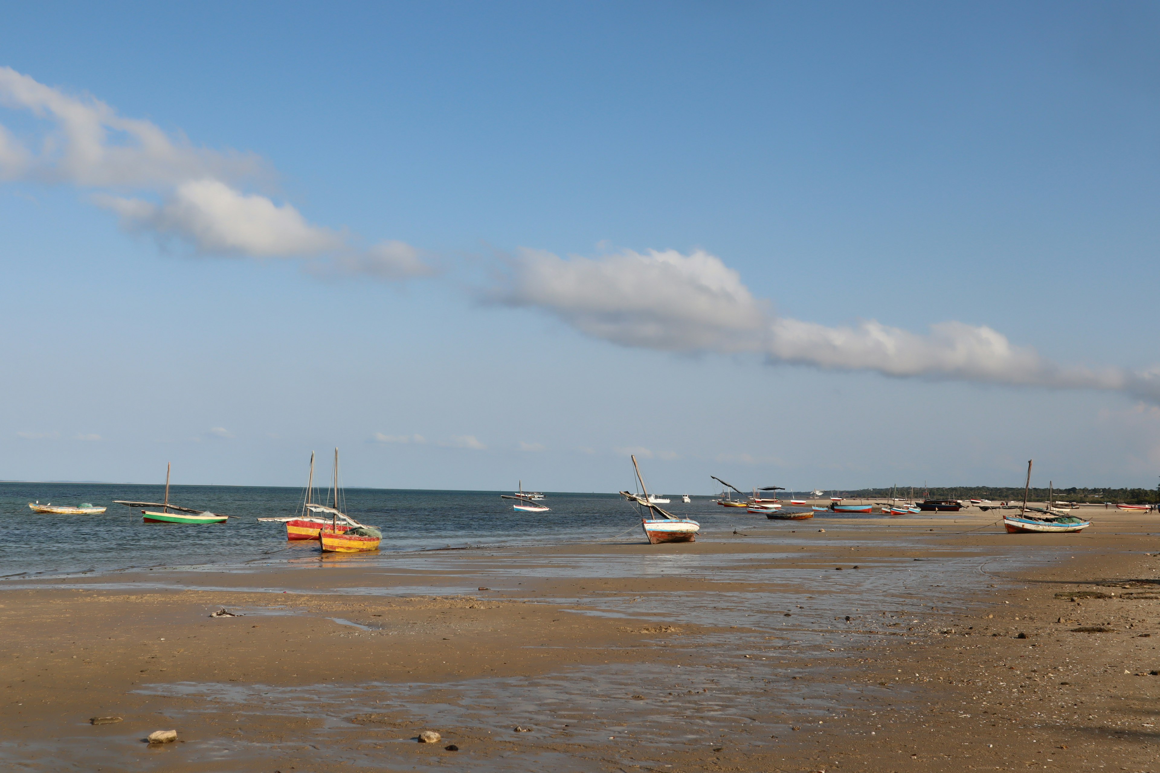 Scenic view of a calm beach with small boats under a blue sky and white clouds