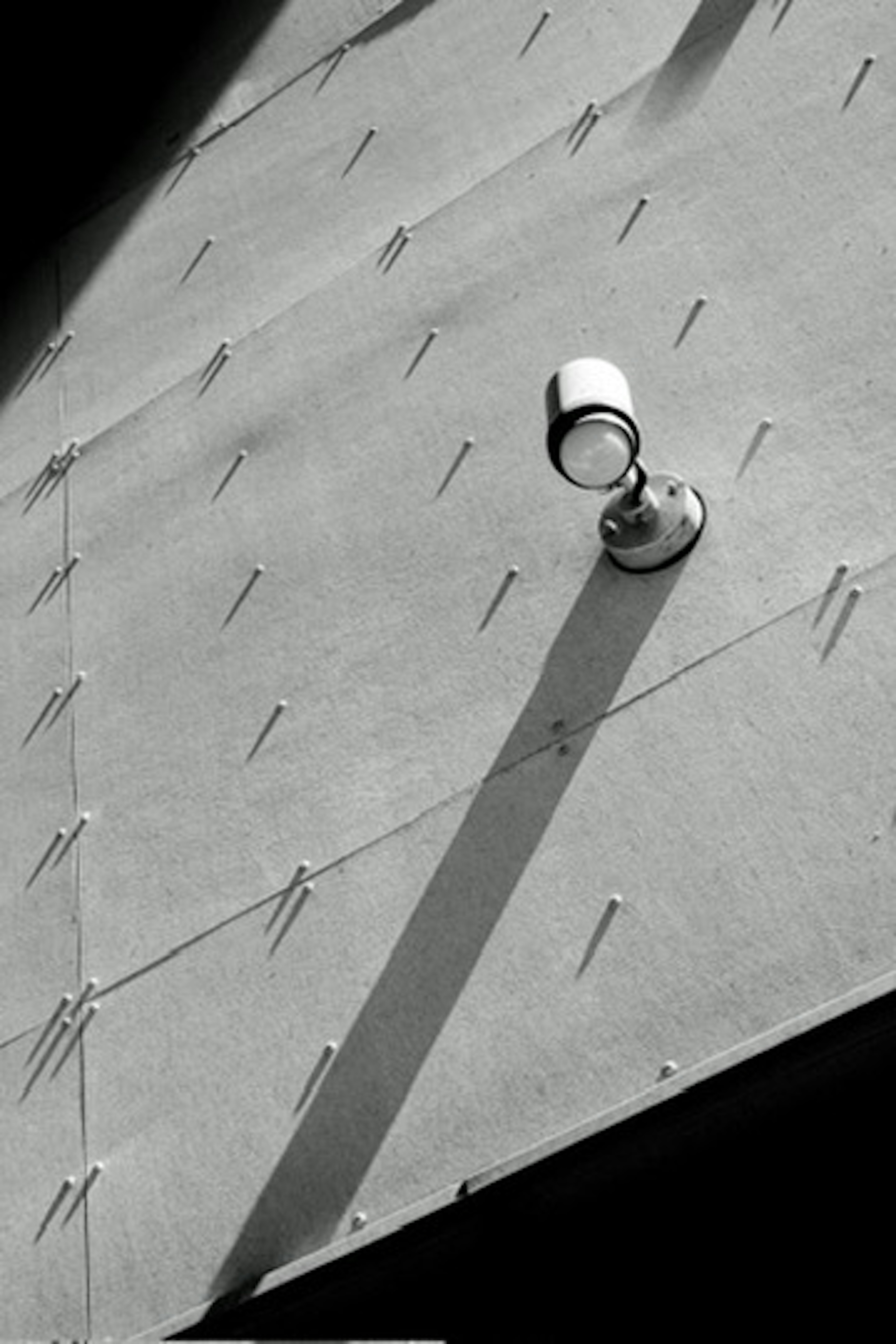 Spotlight mounted on a metallic wall casting a long shadow