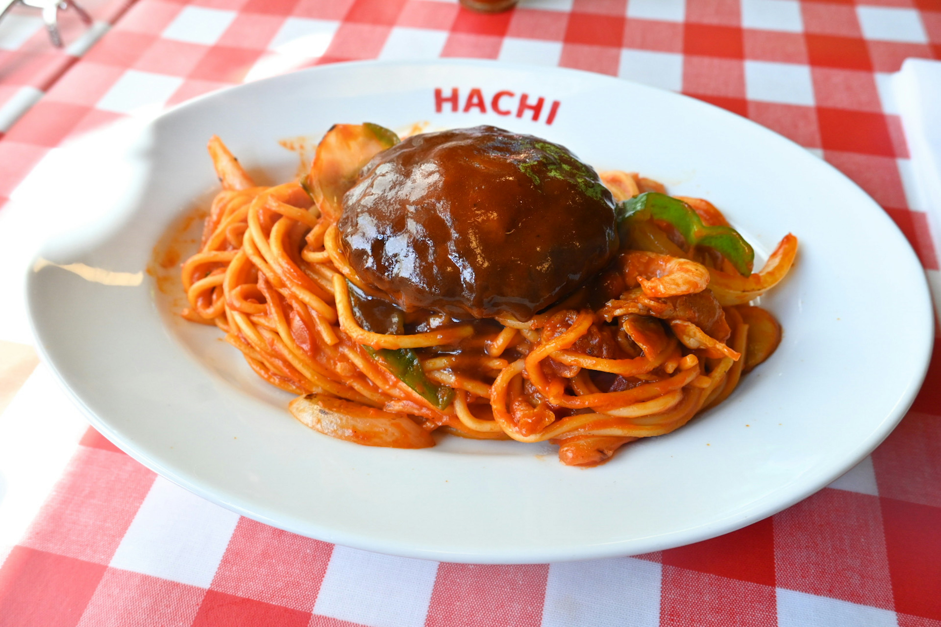 Một đĩa mì spaghetti có bánh hamburger và rau xanh trang trí trên khăn trải bàn kẻ ô đỏ và trắng