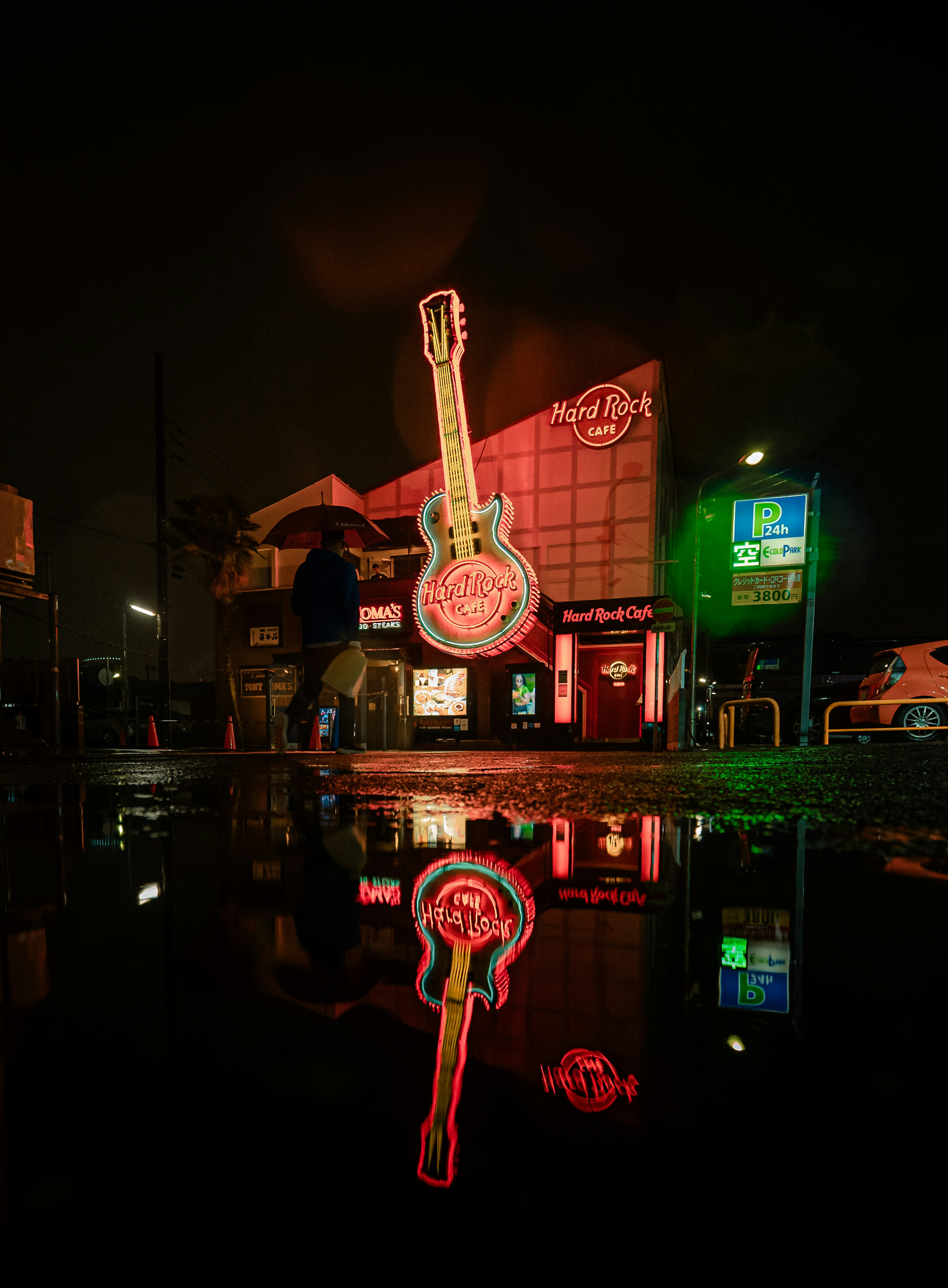 Nachtszene des Hard Rock Cafe Schilds leuchtend mit Neon-Gitarrenreflexion in einer Pfütze