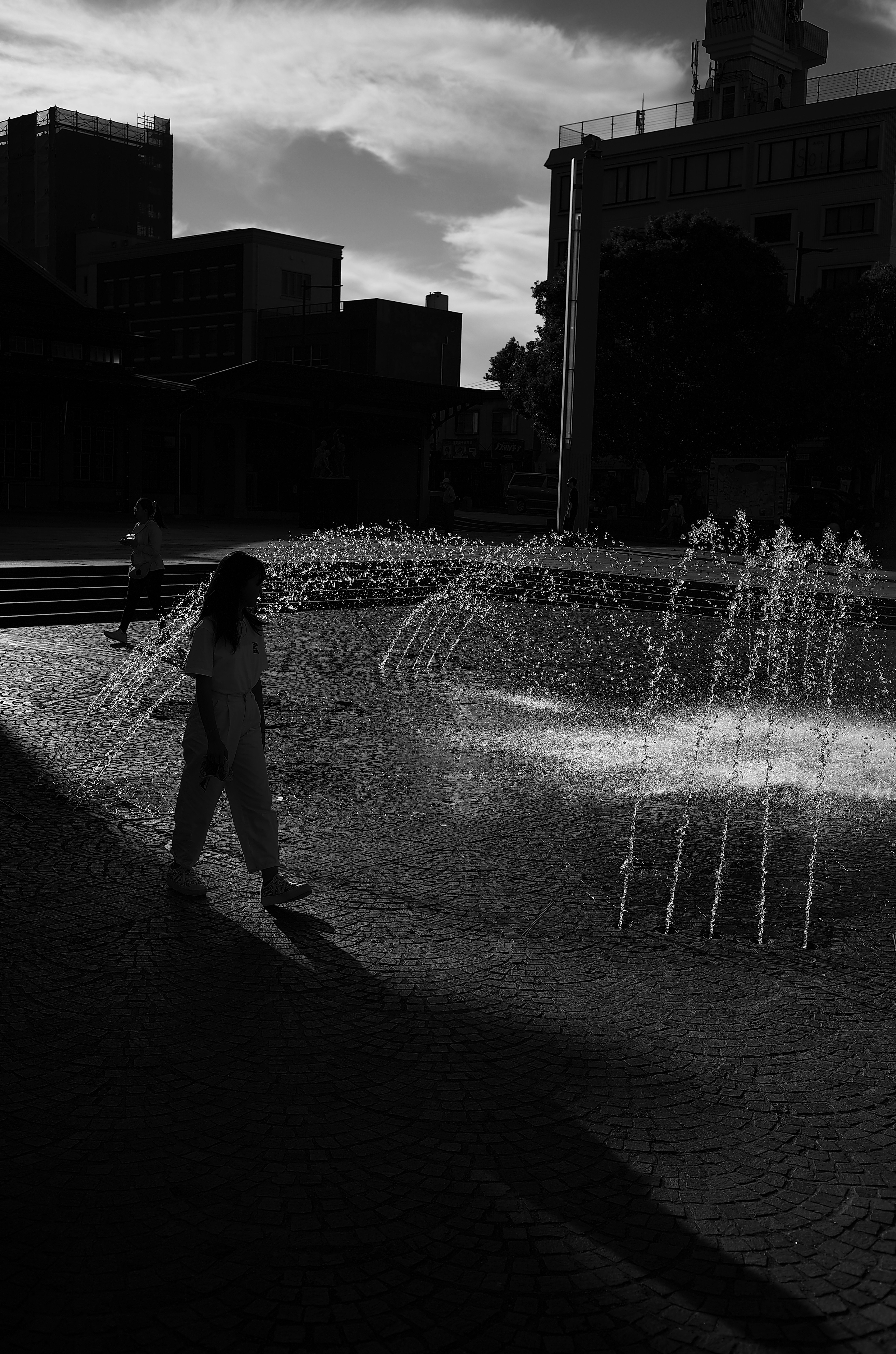 Femme marchant devant une fontaine en noir et blanc avec des ombres