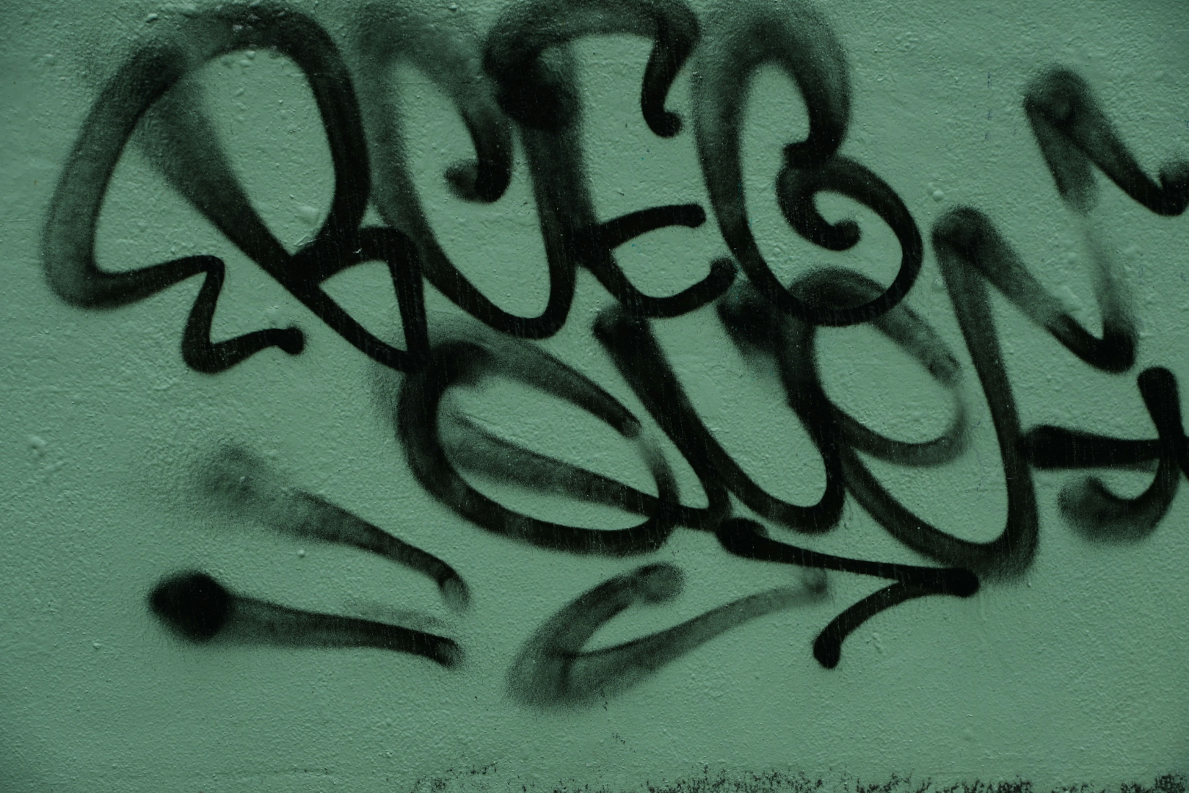 Black graffiti art on a green wall featuring stylized letters